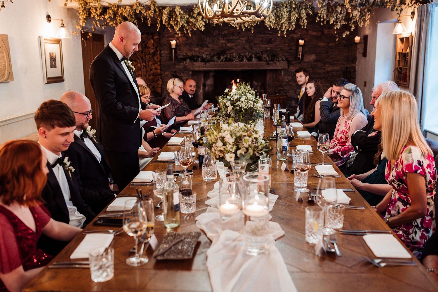 Formal dinner party gathering around an elegantly set table with floral decorations and candlelight.