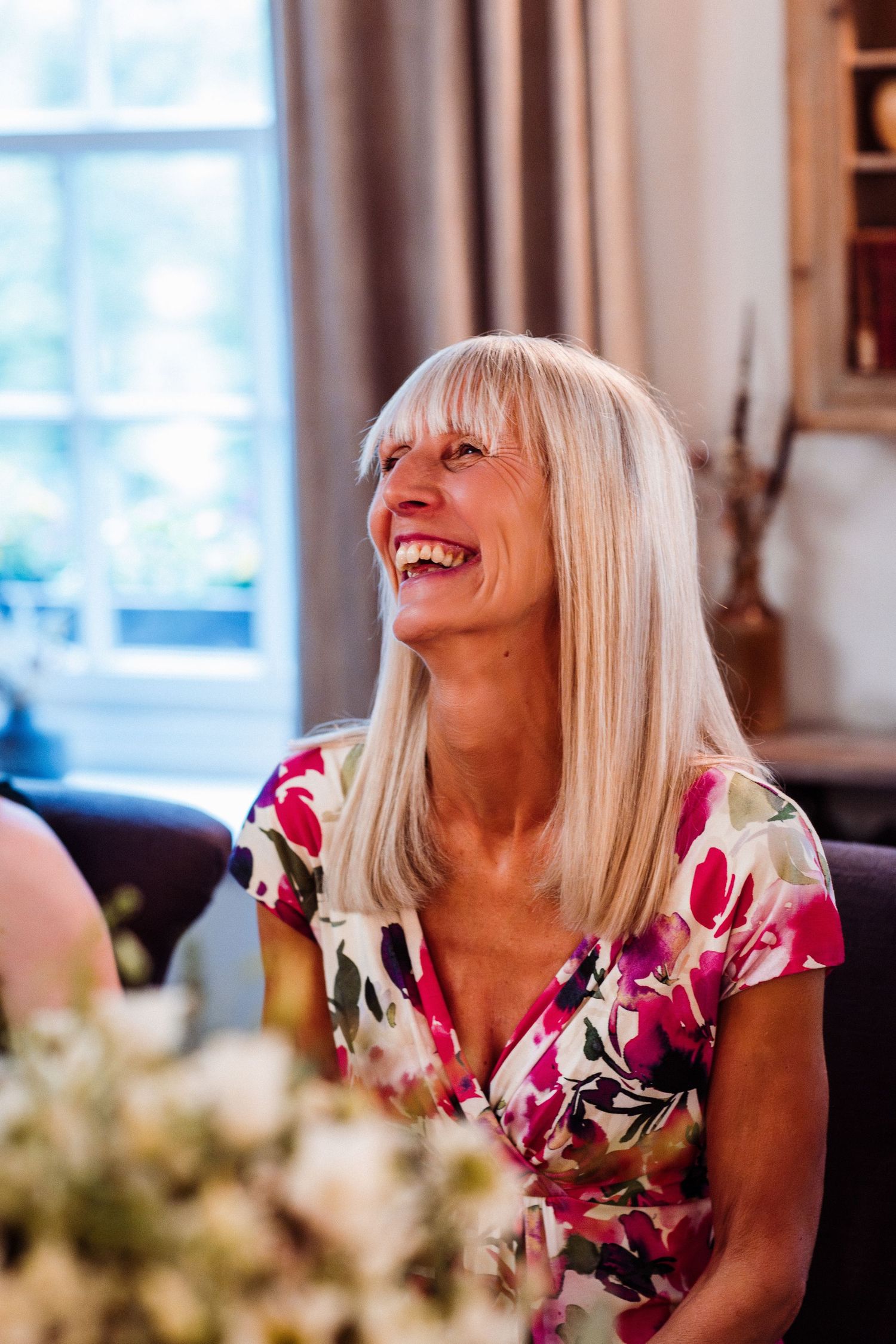 A person in a floral print dress laughs joyfully at a dining table with decorative elements visible.