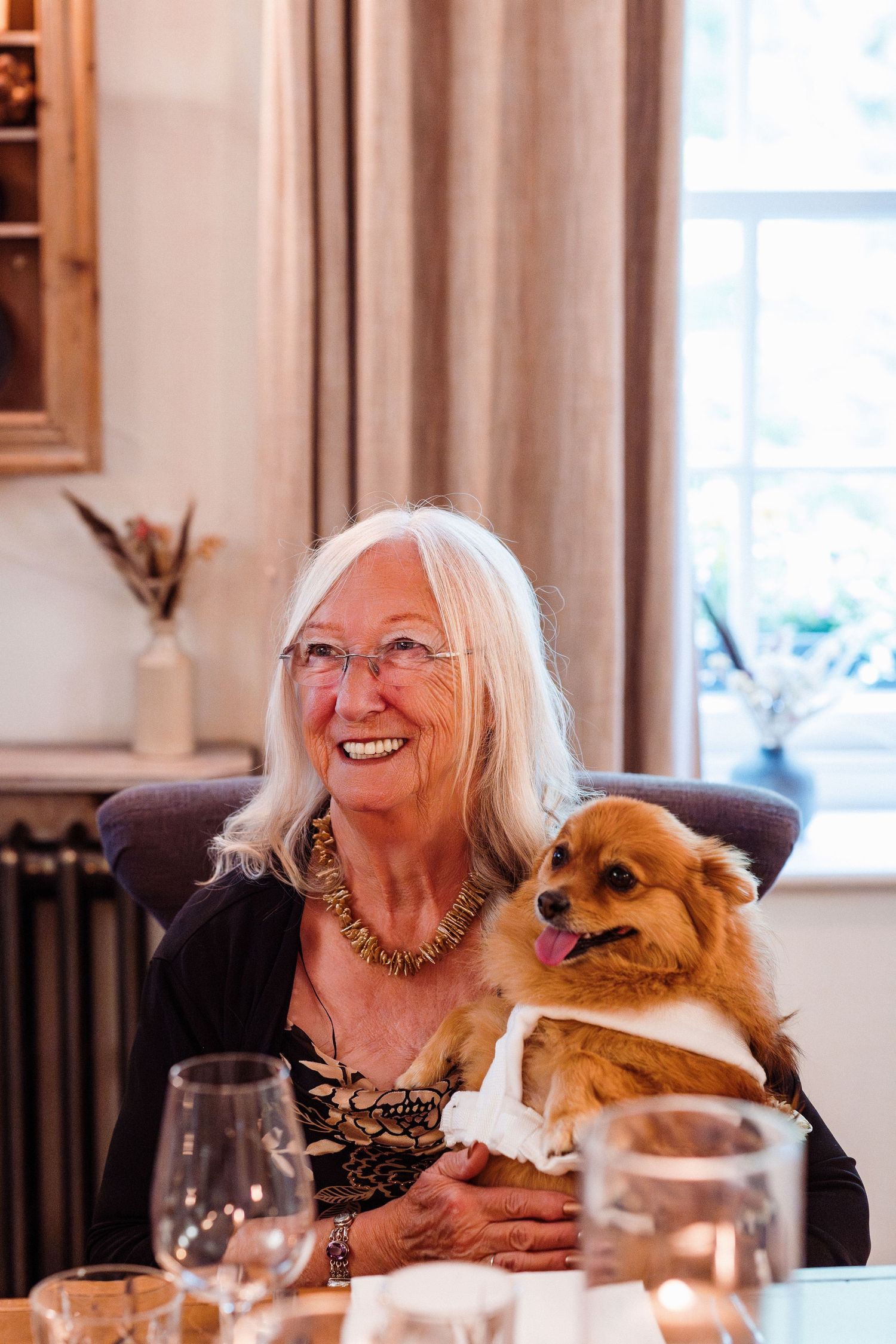 A joyful moment shared between a senior woman and her small brown dog at an elegant dinner table setting.