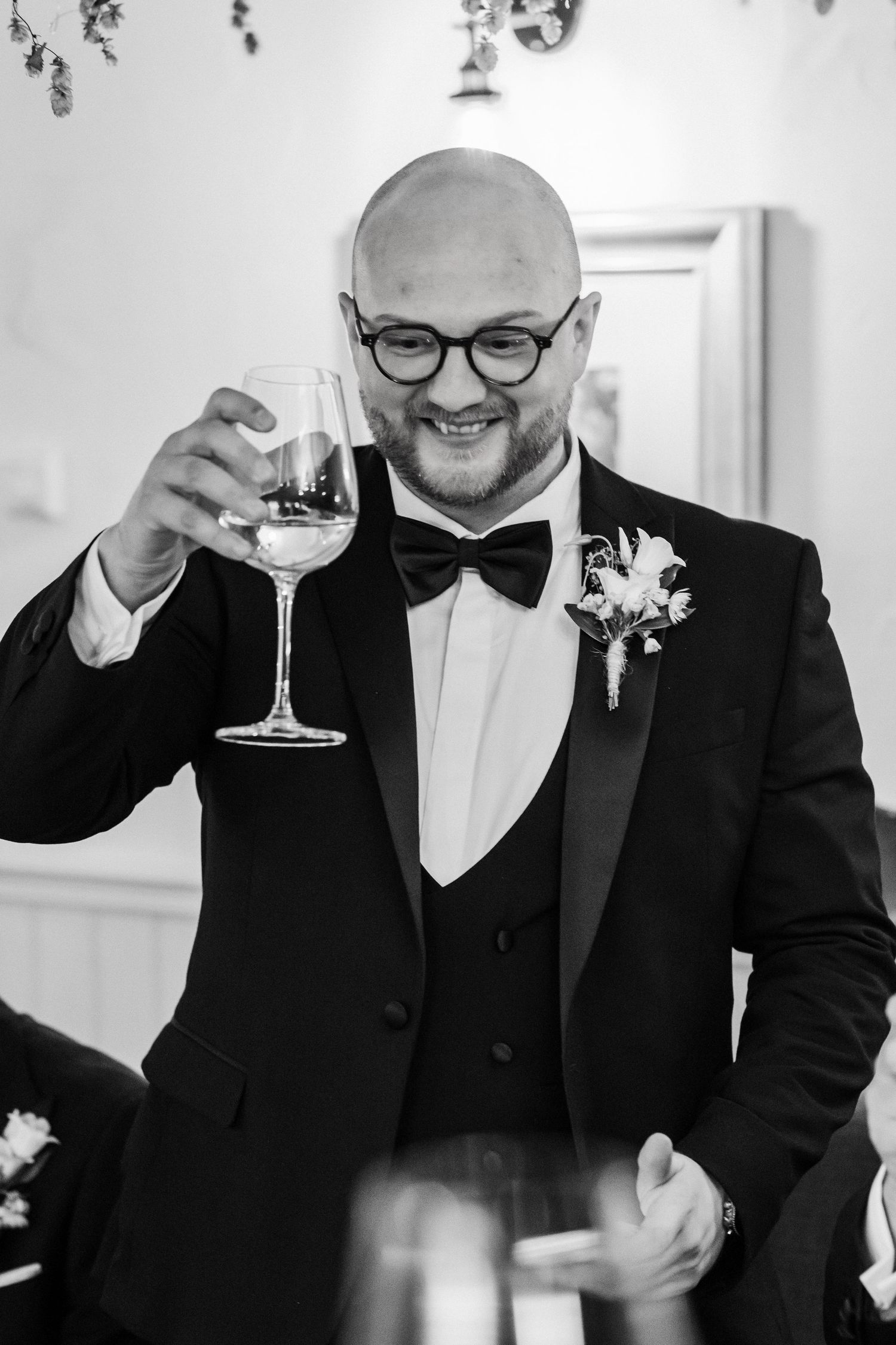 A wedding guest in a black tuxedo and bow tie raises a glass of champagne during a celebration.