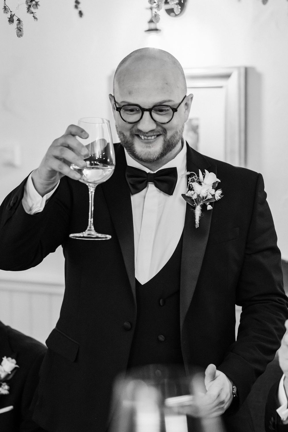 A wedding guest in a black tuxedo and bow tie raises a glass of champagne during a celebration.