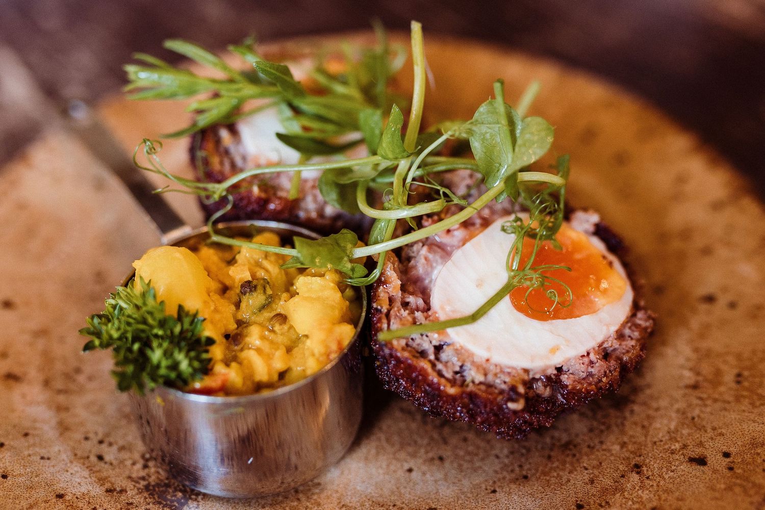 Gourmet plated dish featuring a sunny side up egg garnished with microgreens on a rustic ceramic plate.