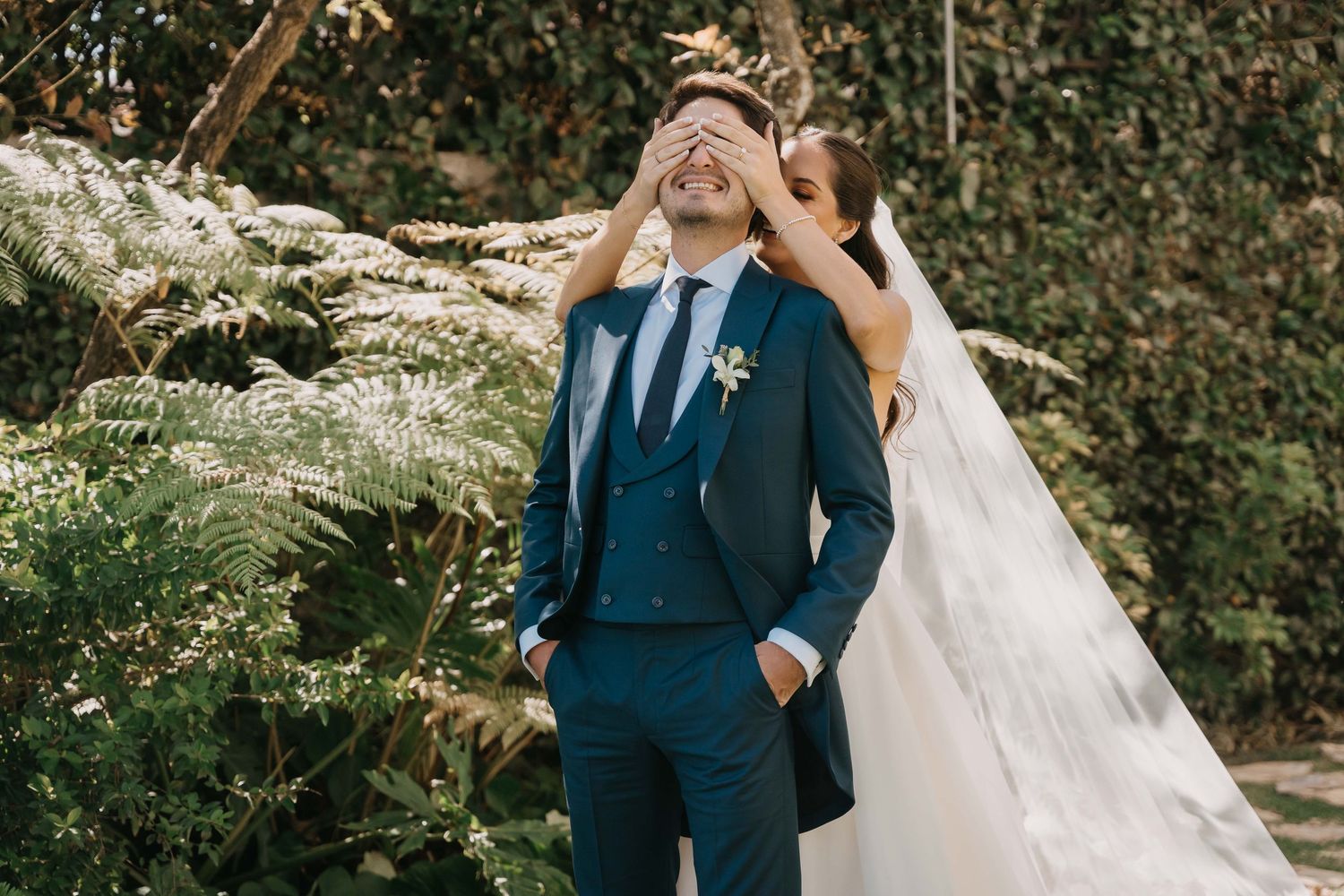 A couple in wedding attire walks hand in hand through a lush garden setting on their special day.