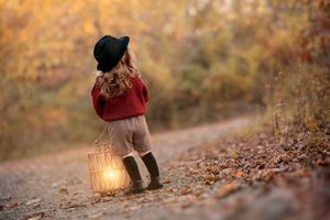 A person in autumn attire sits on a fallen log holding a glowing lantern in a forest filled with golden leaves.