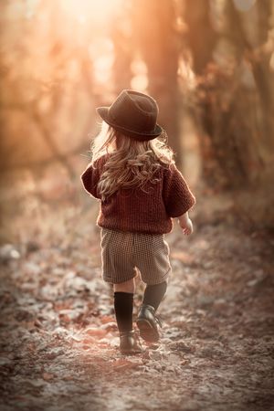 A small toddler wearing brown clothing walks through fallen autumn leaves in a dreamy sepia-toned setting.