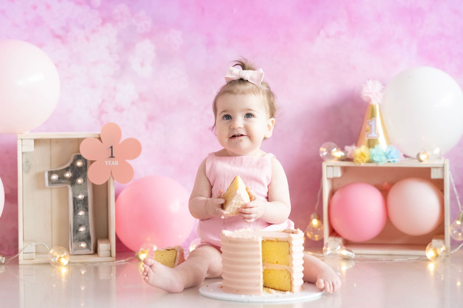 Pink themed cake smash photo session with balloons and party decorations.