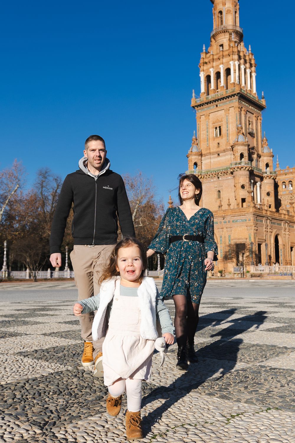 People walking on cobblestone plaza in front of historic church tower with blue sky on sunny winter day.