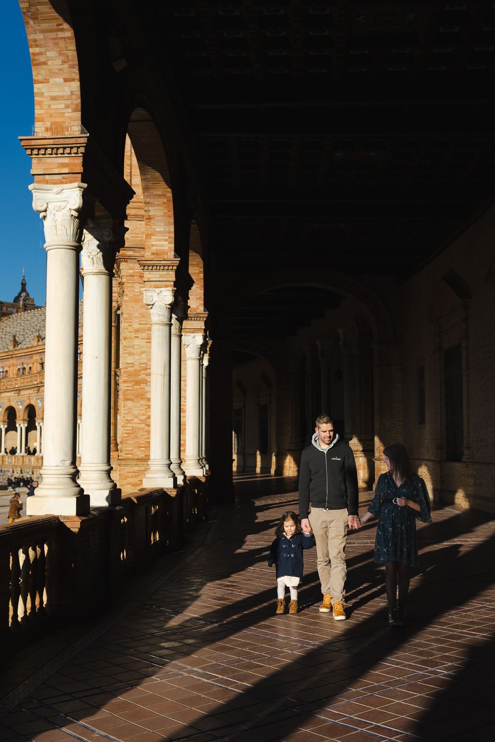 Sunlight casts dramatic shadows through arched columns in a historic Spanish-style colonnade walkway.