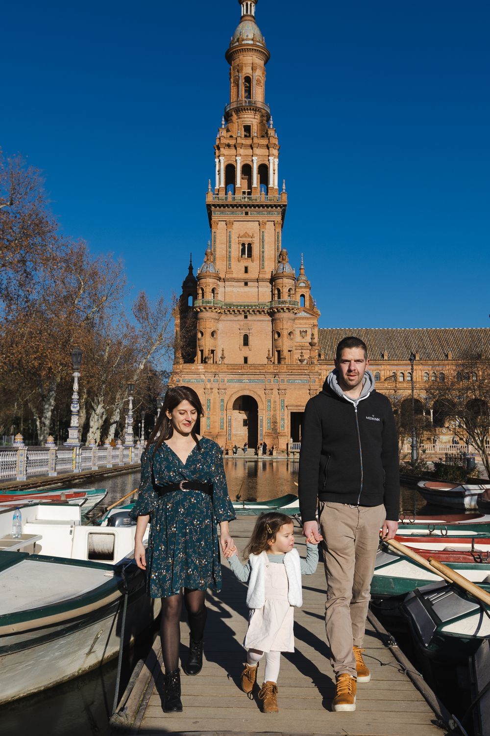 People enjoying a sunny day at Plaza de España in Seville with its iconic architecture and boats in the foreground.
