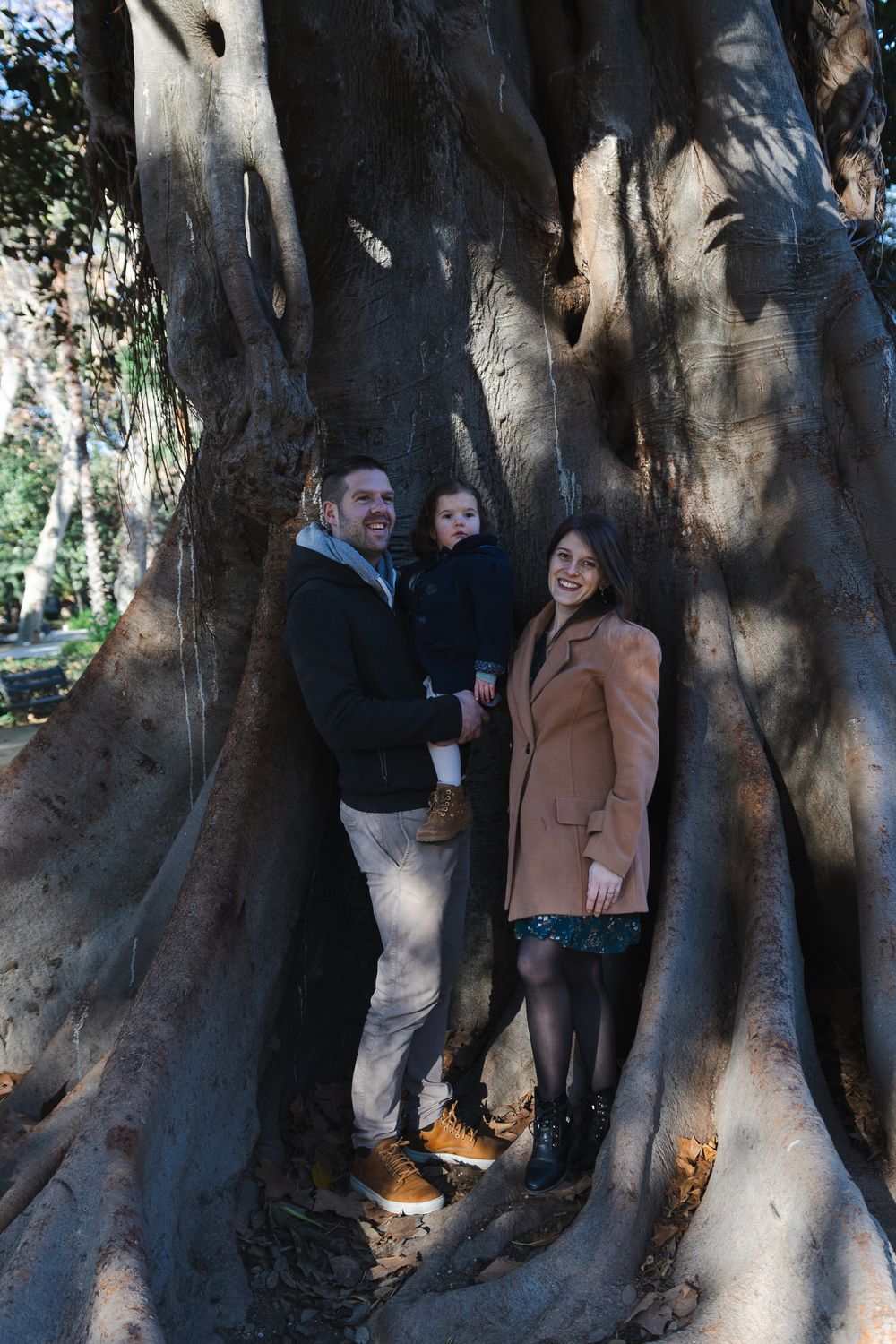 A group of people stand together near the massive trunk of an ancient tree in dappled sunlight.