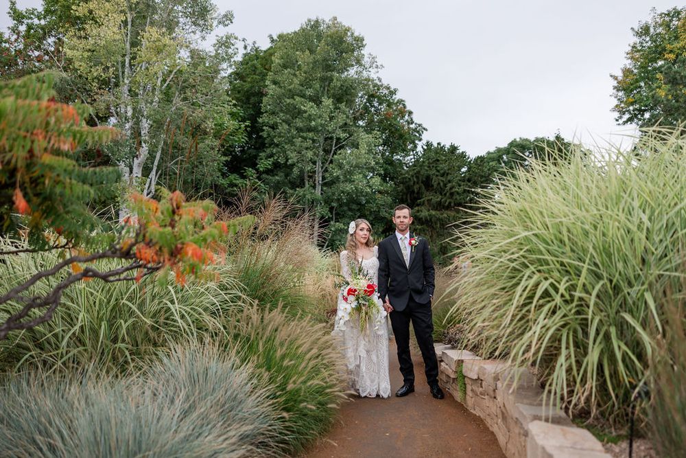 Wedding party poses in a lush garden path lined with ornamental grasses and autumn foliage.