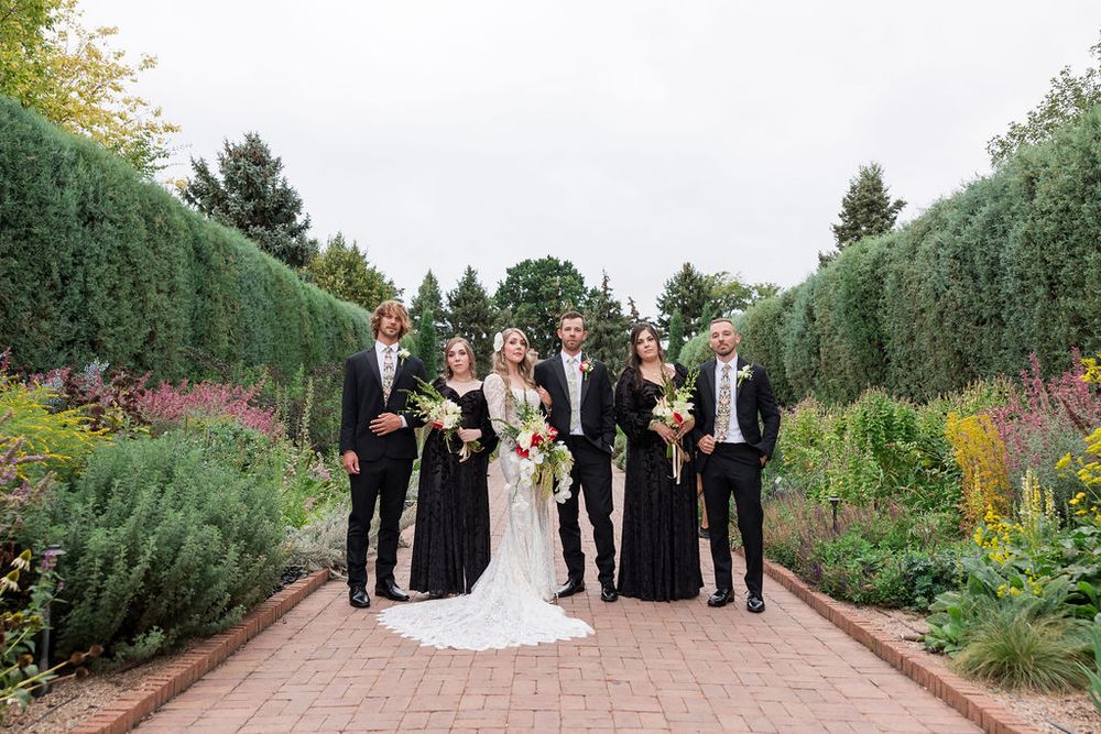 Wedding group stands together on a brick pathway surrounded by tall ornamental grasses and greenery.