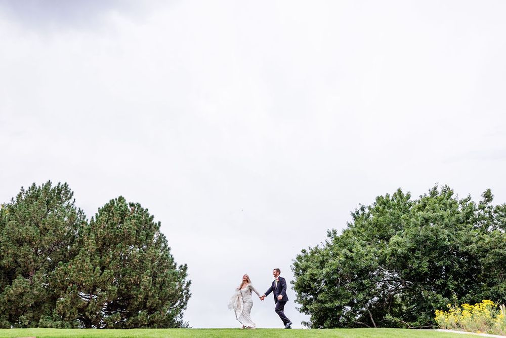 Outdoor wedding ceremony with couple exchanging rings in front of guests under green trees.