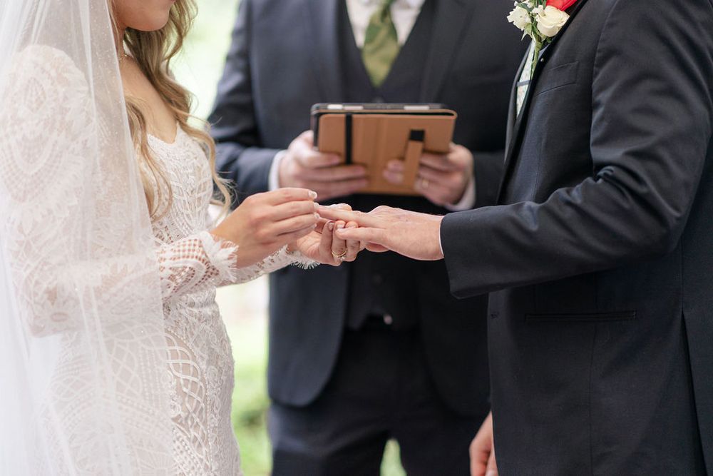 Close-up of wedding ring exchange between couple during outdoor ceremony.