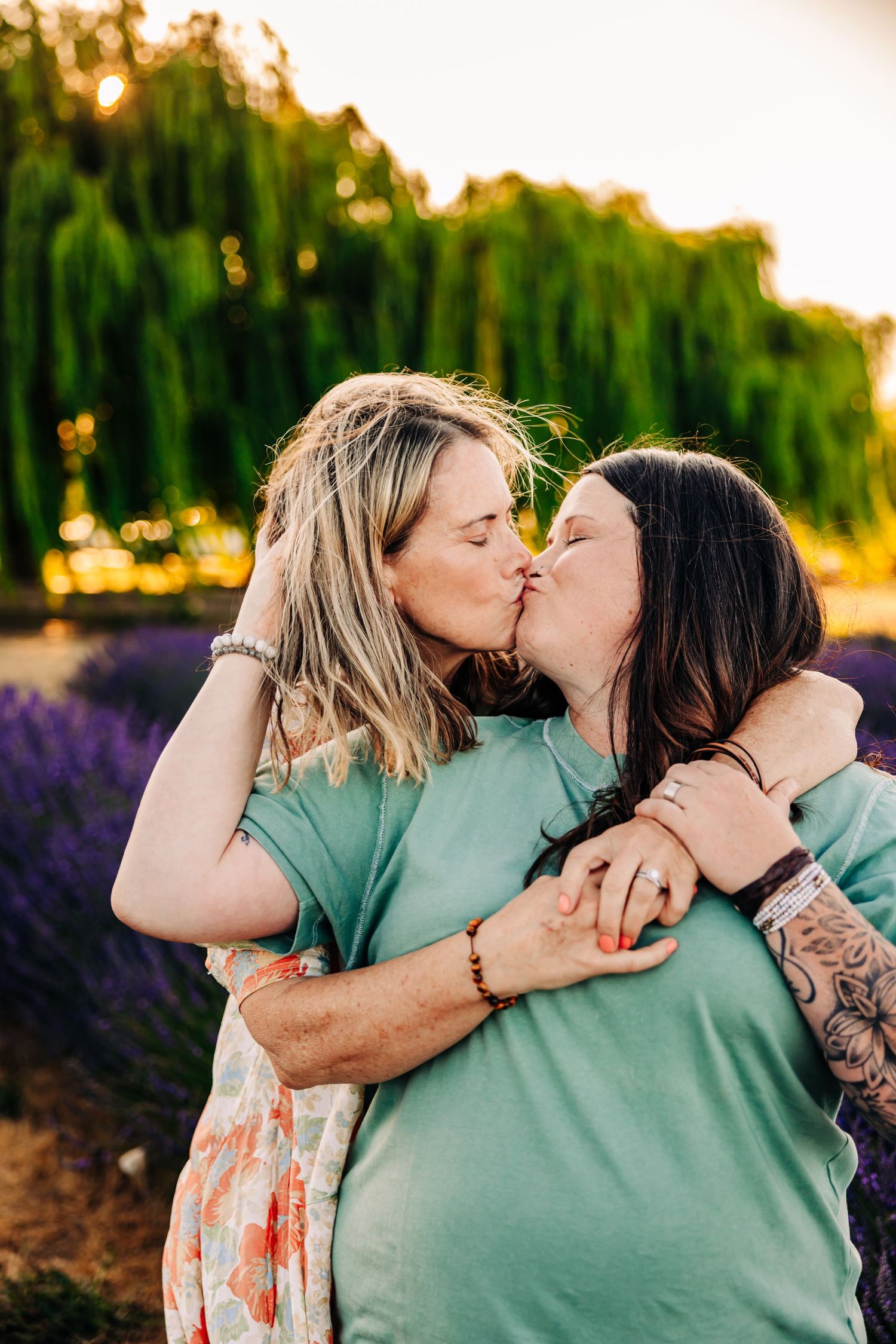 A romantic couple embraces and kisses in a lavender field at sunset wearing matching mint green outfits.
