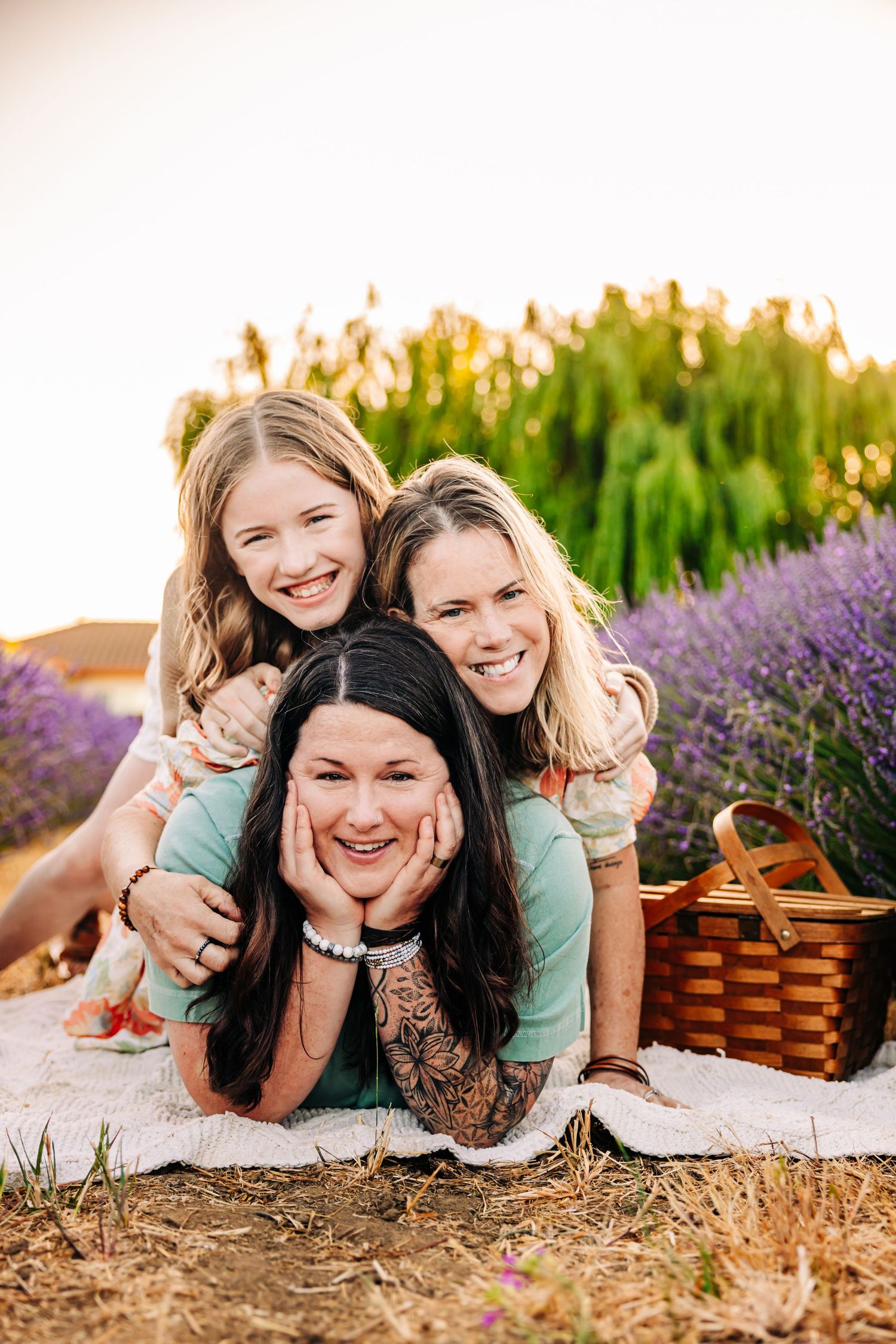 Family members lying on a blanket in a lavender field at sunset with a picnic basket nearby.