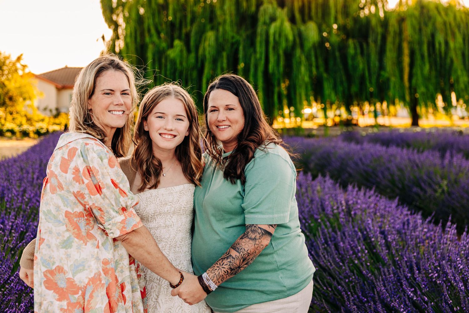 Three people laughing together in a vibrant purple lavender field at sunset.