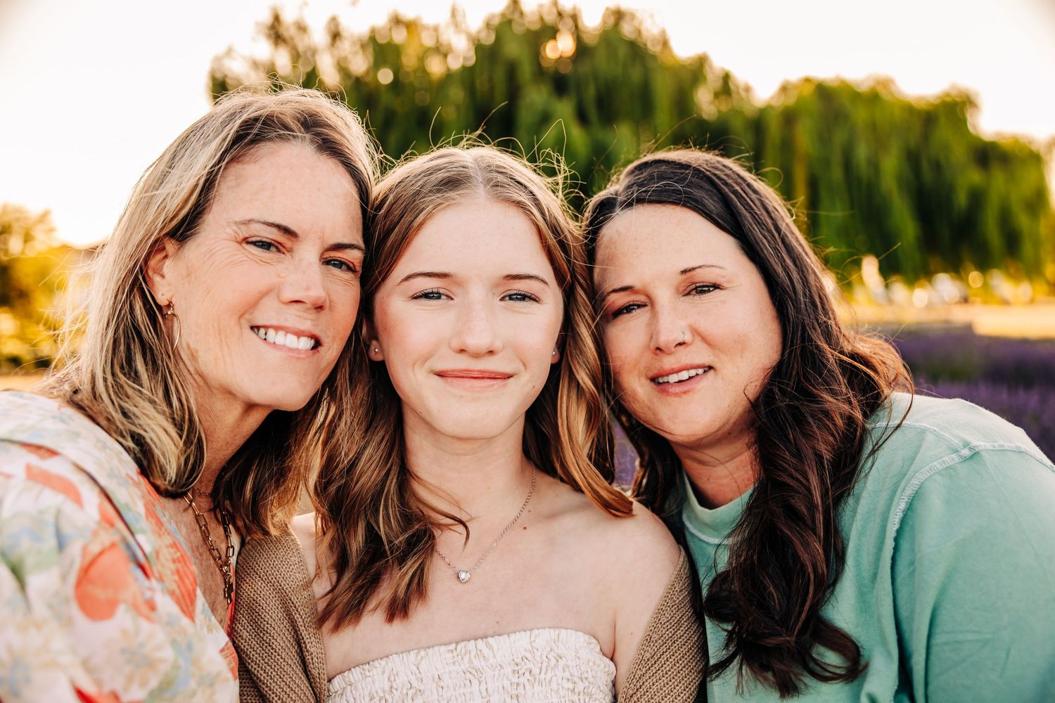 Three people smiling together outdoors during golden hour with trees in the background.