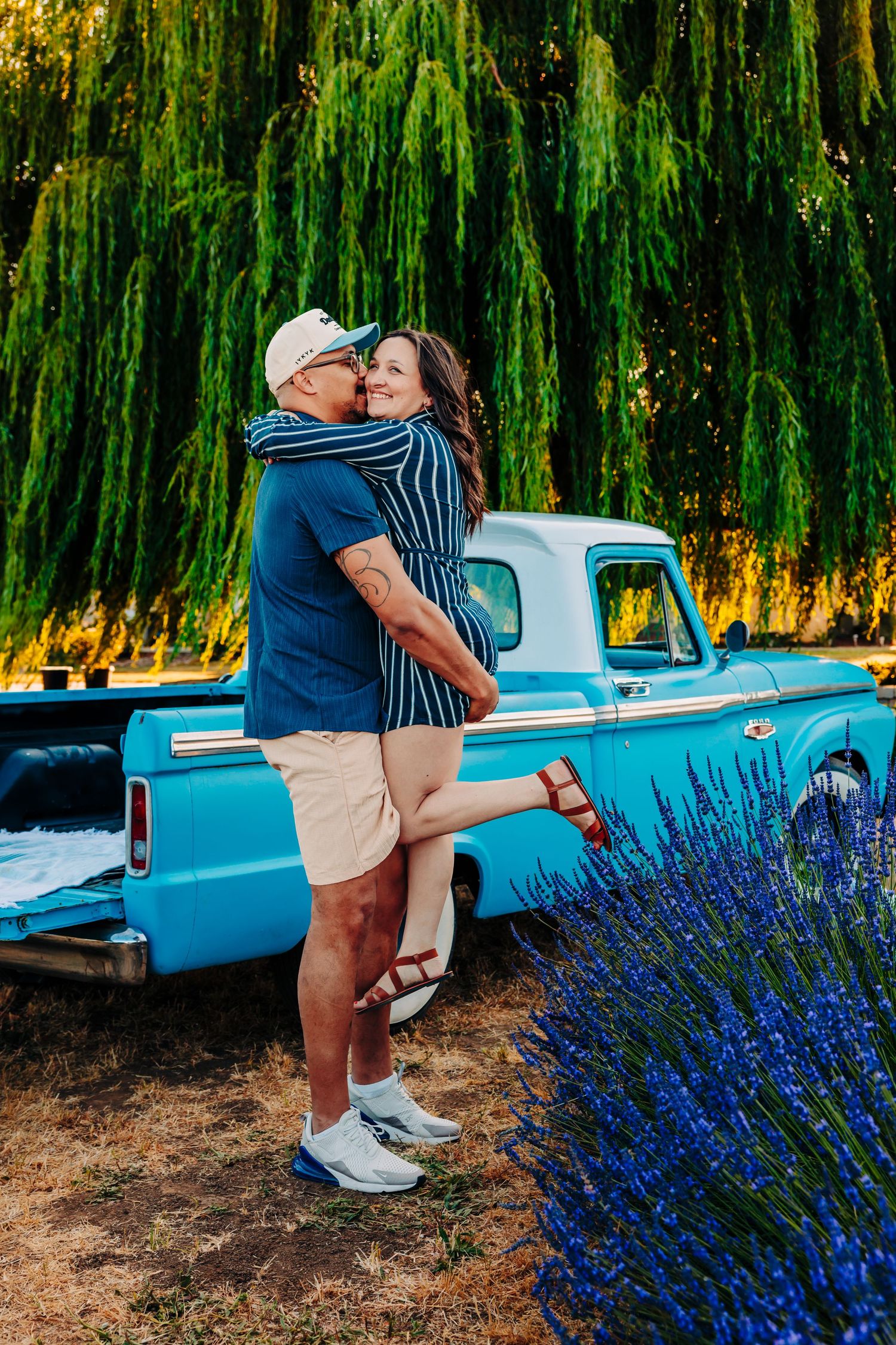 A romantic couple poses next to a vintage blue car with blooming lavender flowers in the foreground.