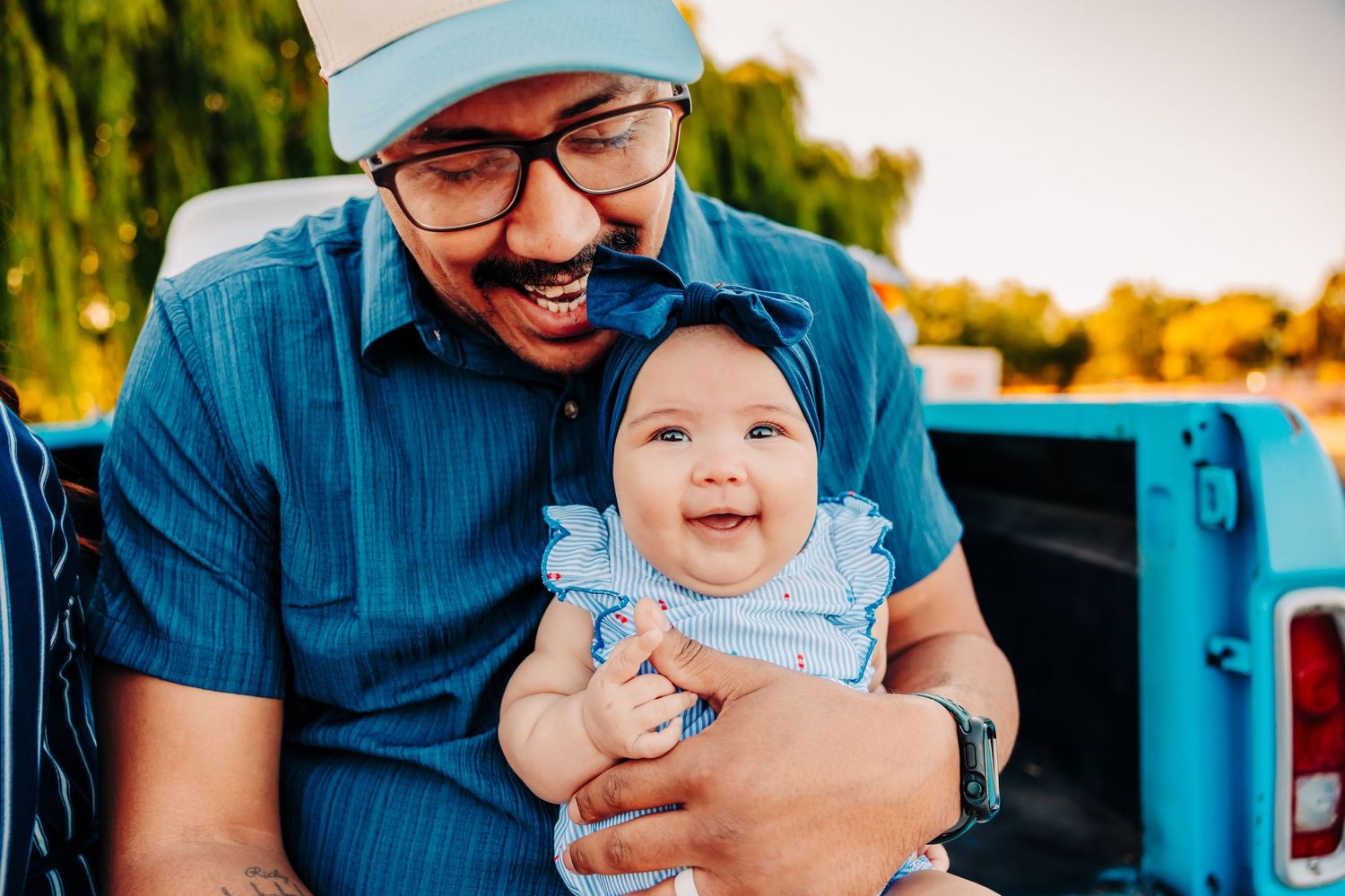 A joyful parent and baby share a heartwarming moment together while sitting in the bed of a blue pickup truck.