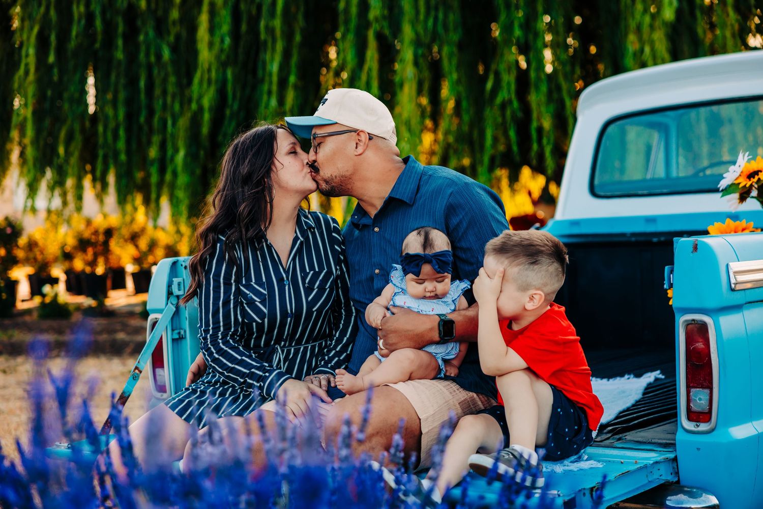 Family enjoying a summer picnic together near a vintage blue truck at sunset in a park setting.