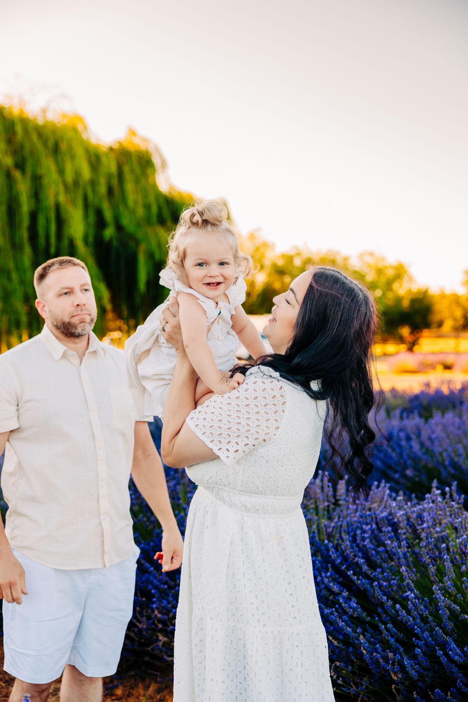 Family wearing white outfits poses together in a blooming lavender field at sunset.