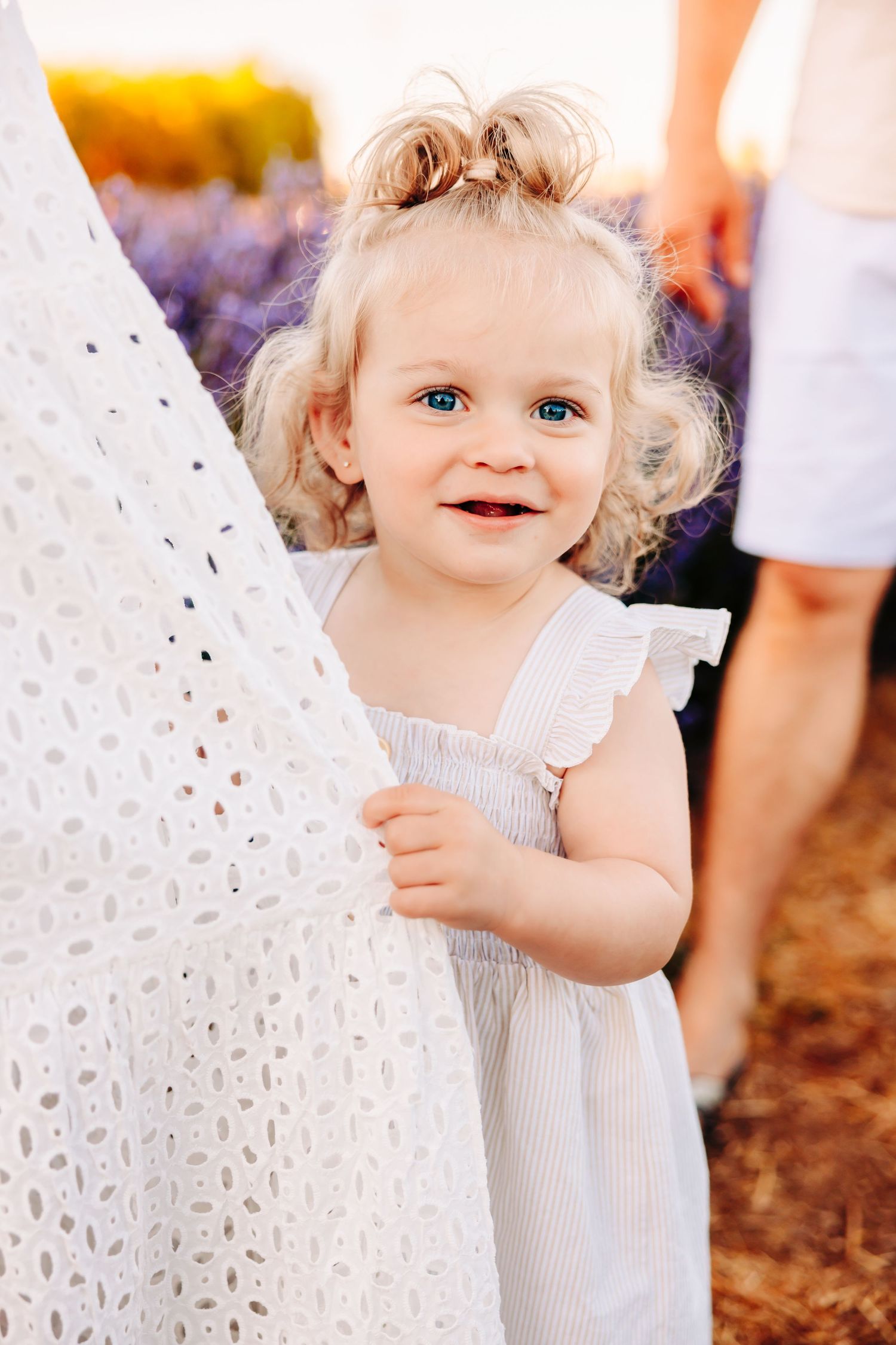 A small child in a white dress holds a delicate white lace parasol outdoors.