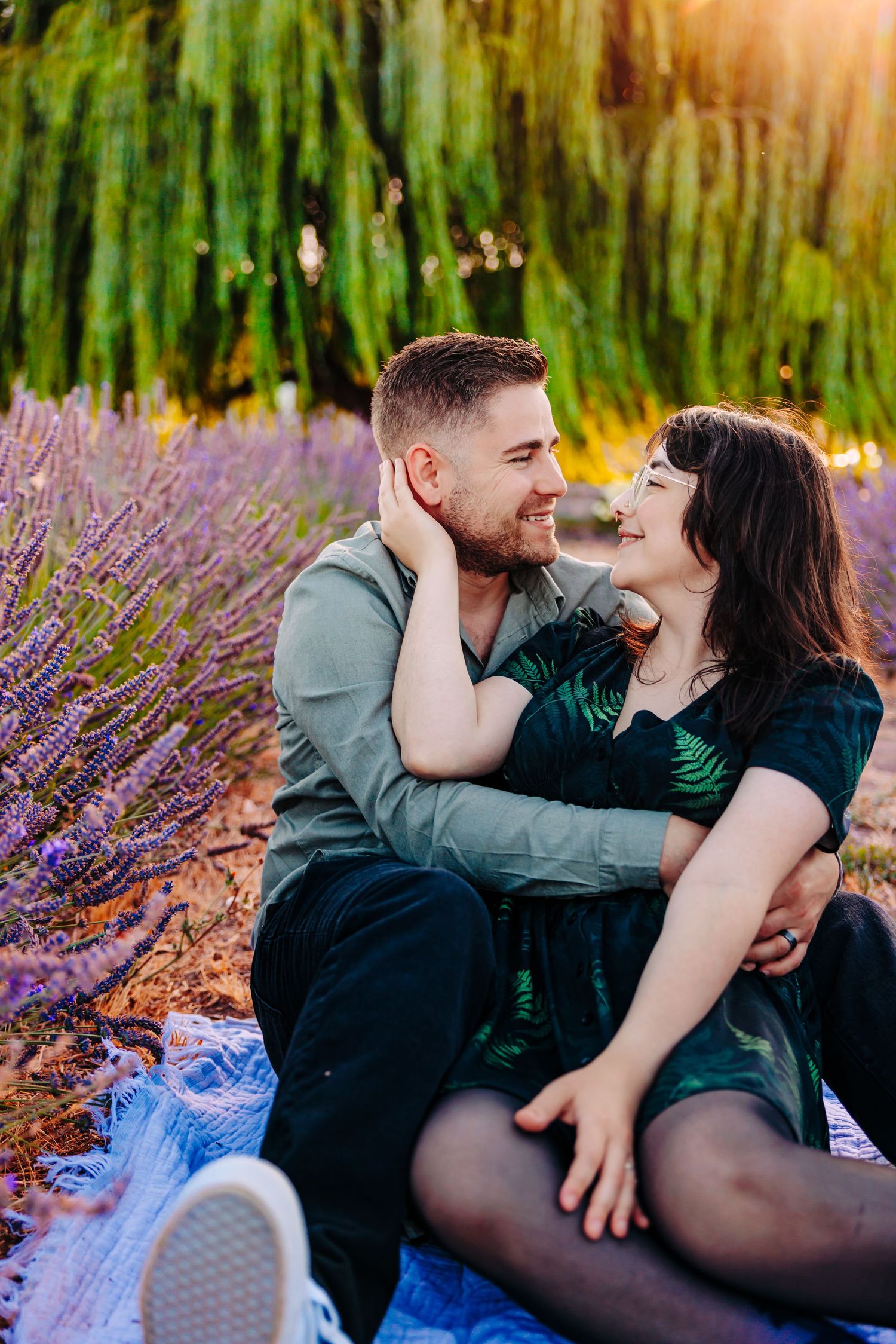 Romantic couple sharing an intimate moment while sitting on a blanket in a blooming lavender field at sunset.