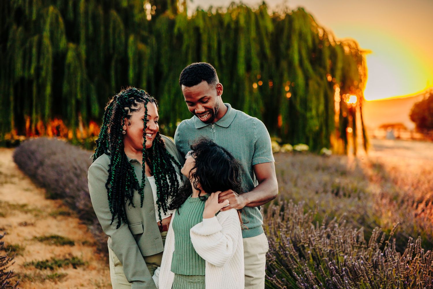 A loving family shares a joyful moment together at sunset with willow trees in the background.