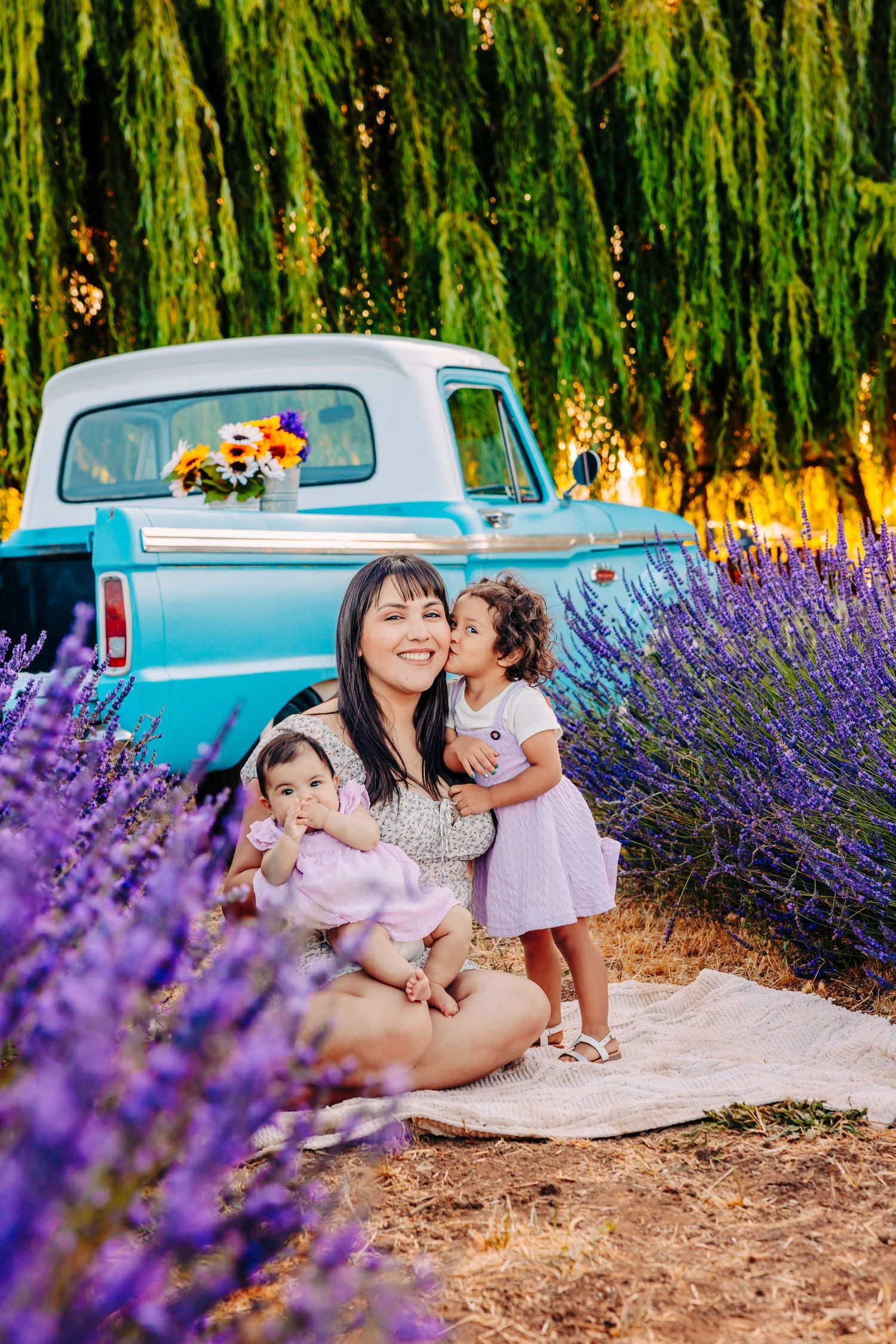A family enjoys a summer photoshoot in a lavender field next to a vintage blue car on a sunny day.