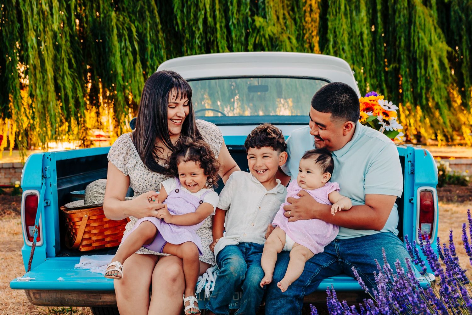 A family sits together on a blanket in a park with a vintage turquoise truck in the background during golden hour.