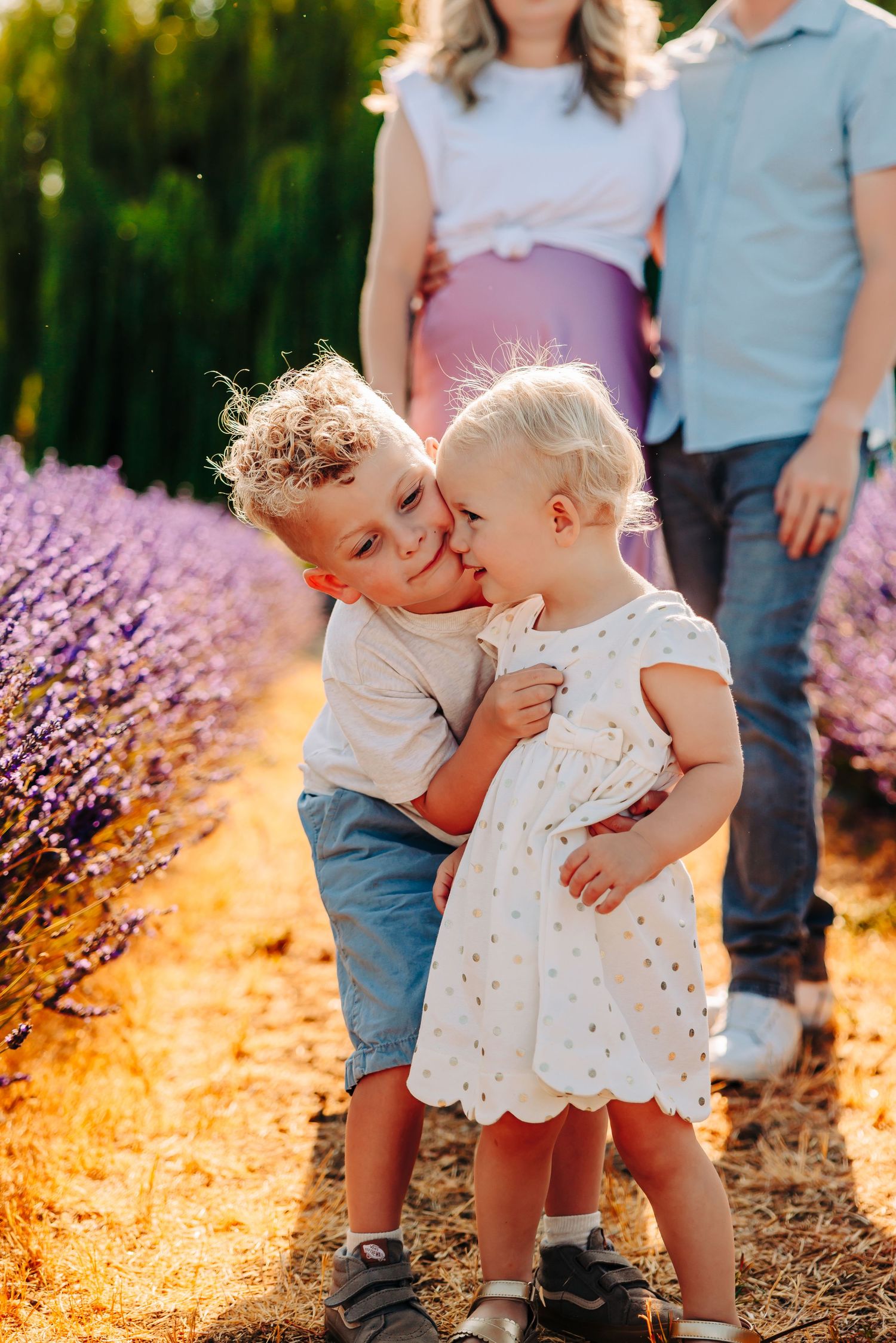 Two toddlers in white dresses share sweet moments together in a lavender field at sunset.