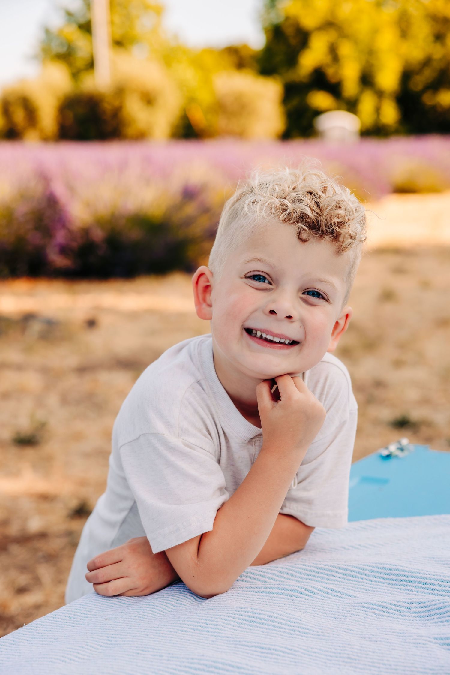 A young child smiles while resting on a blanket outdoors during golden hour.