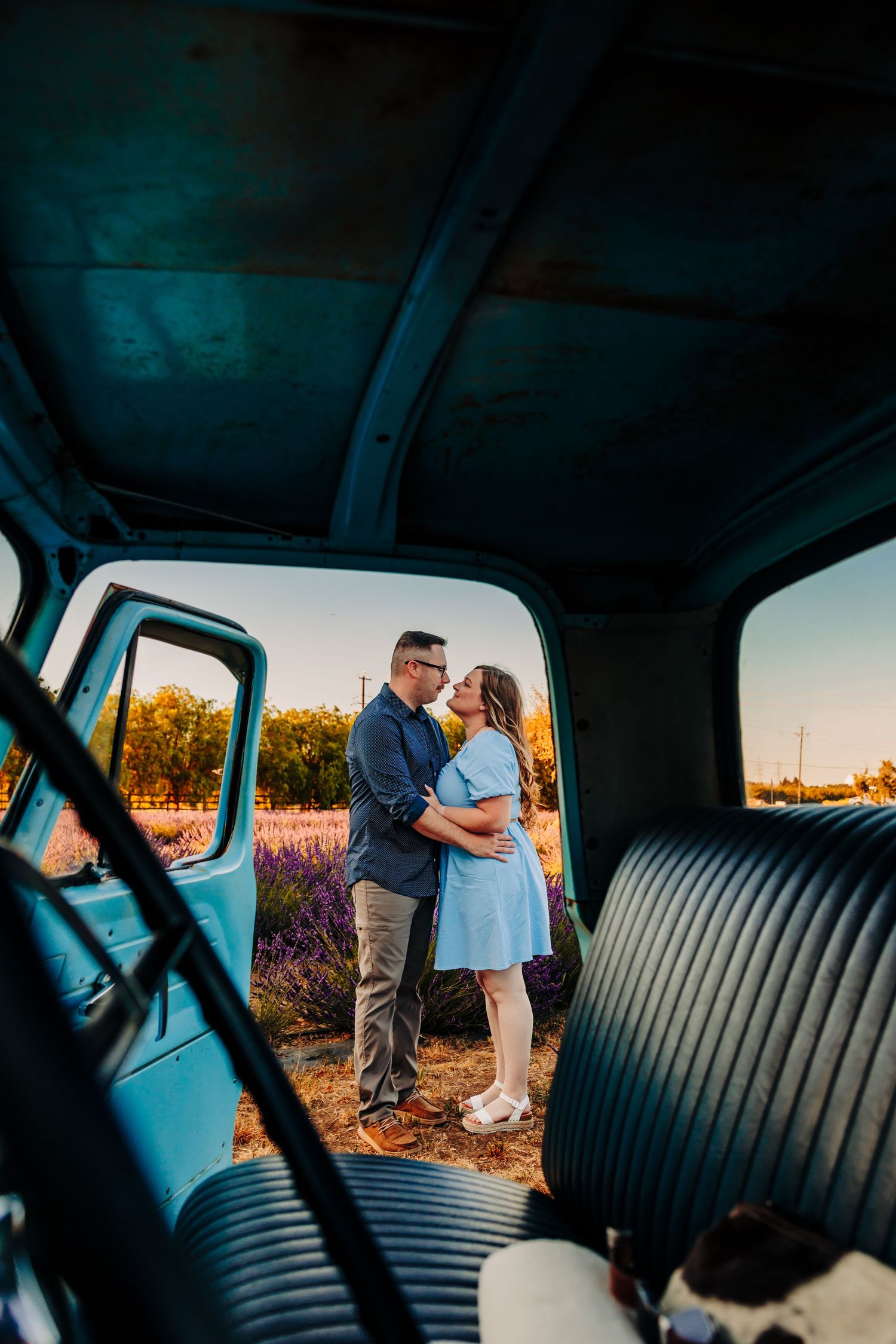 A couple shares an intimate moment at sunset viewed through a vintage car interior with leather seats.