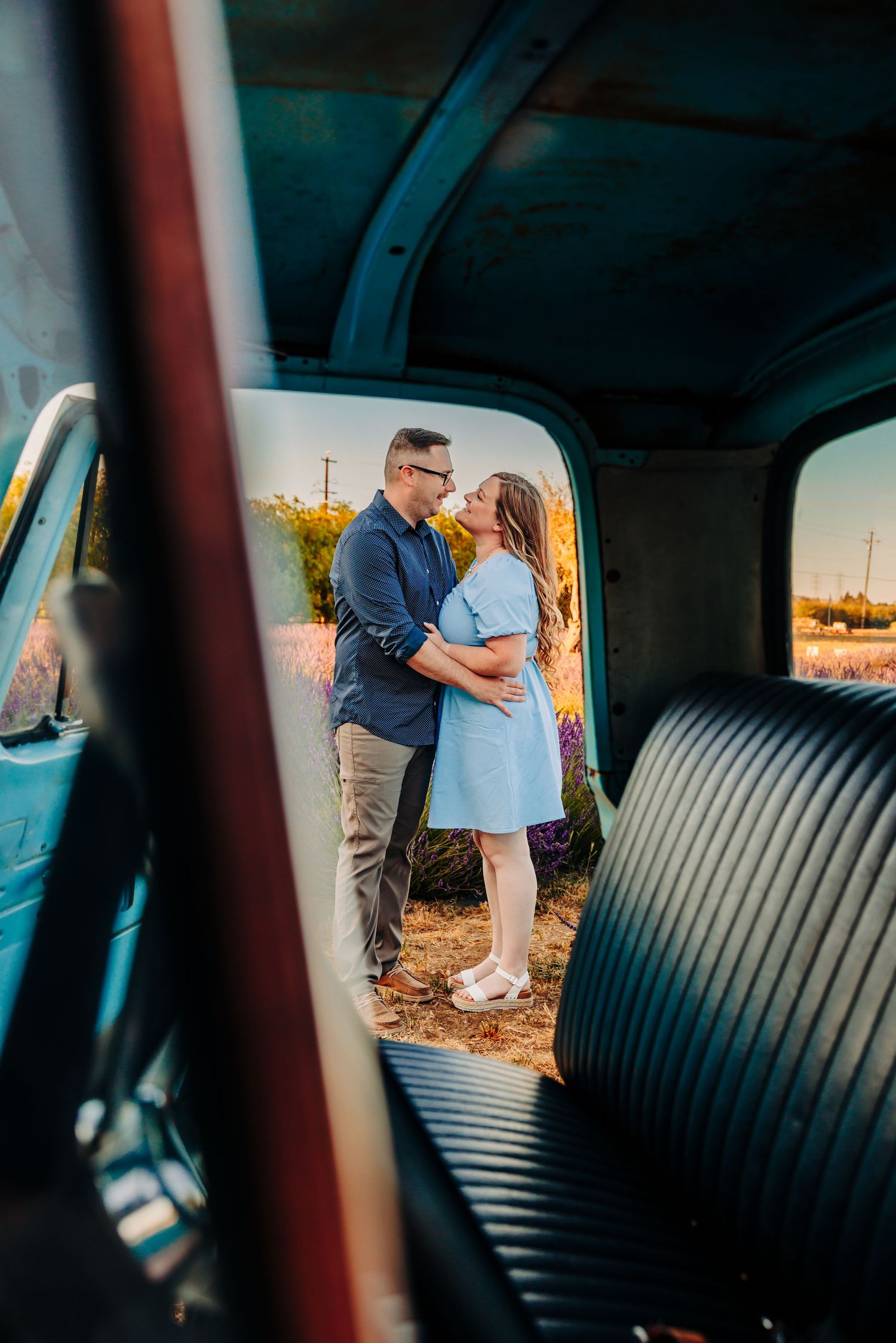 Romantic couple embraces at sunset viewed through vintage car window with leather bench seats.