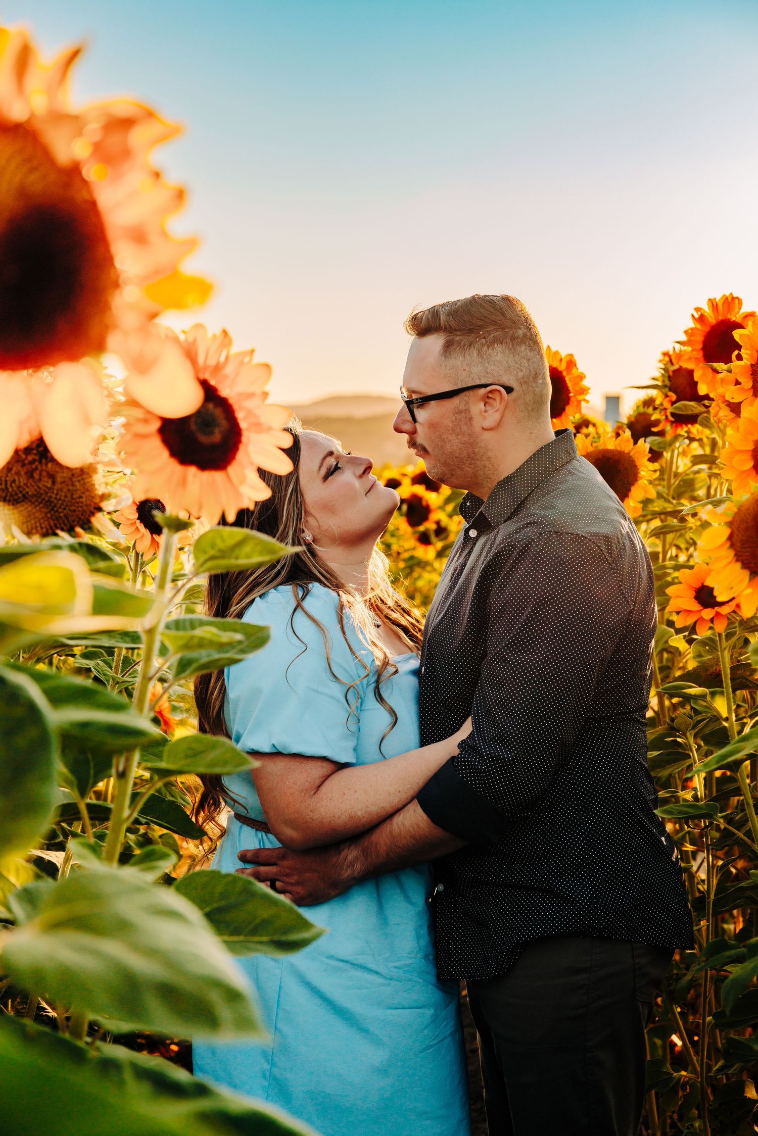 A romantic couple embraces among blooming sunflowers at sunset creating a dreamy outdoor portrait session.