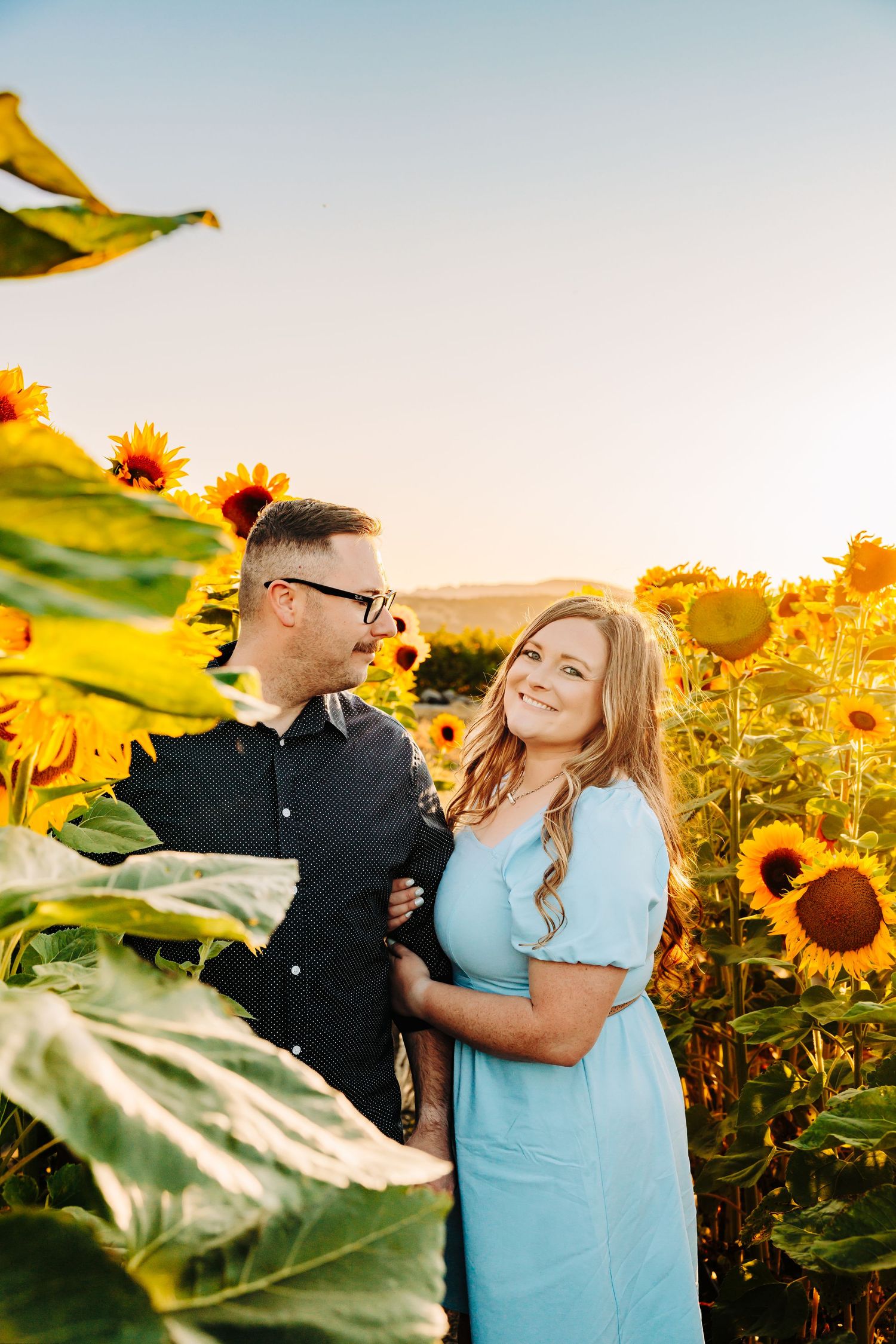 A couple shares joyful moments together in a vibrant sunflower field during golden hour.