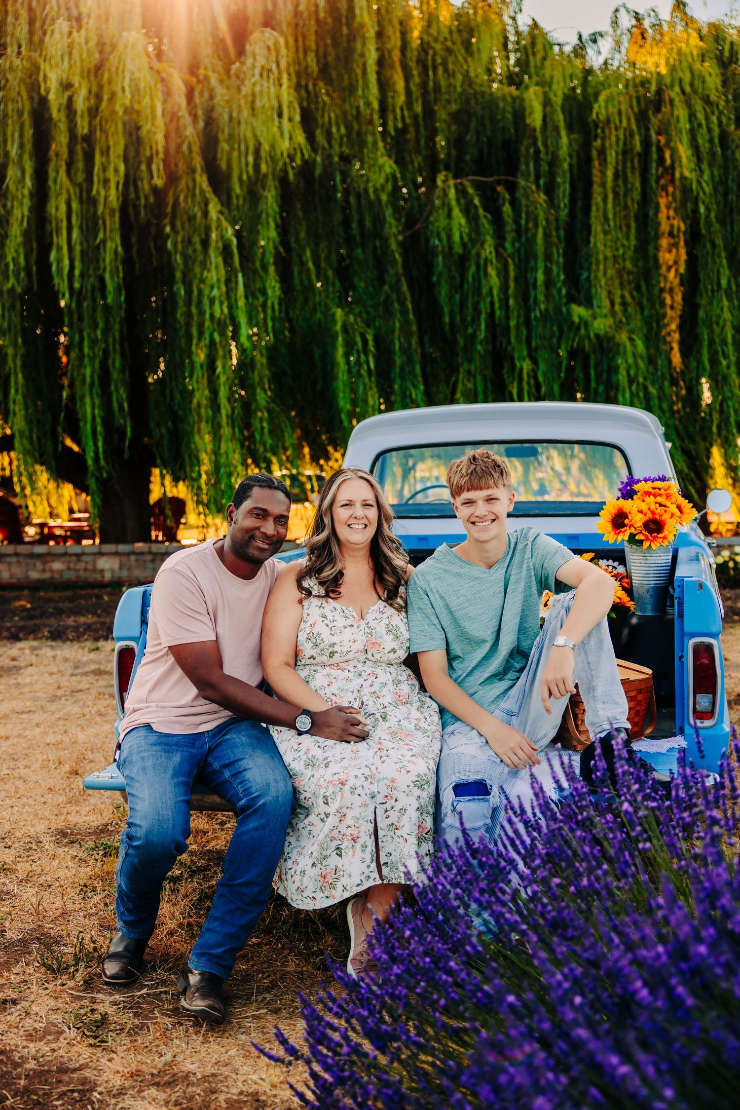 A group poses together against a backdrop of vibrant purple lavender and a vintage blue pickup truck at sunset.