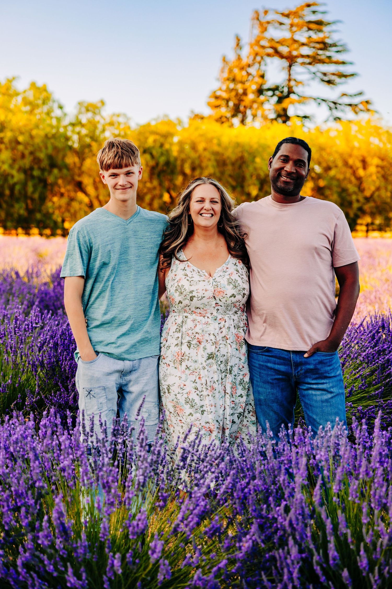 A group poses together in a vibrant lavender field during golden hour with autumn trees in the background.