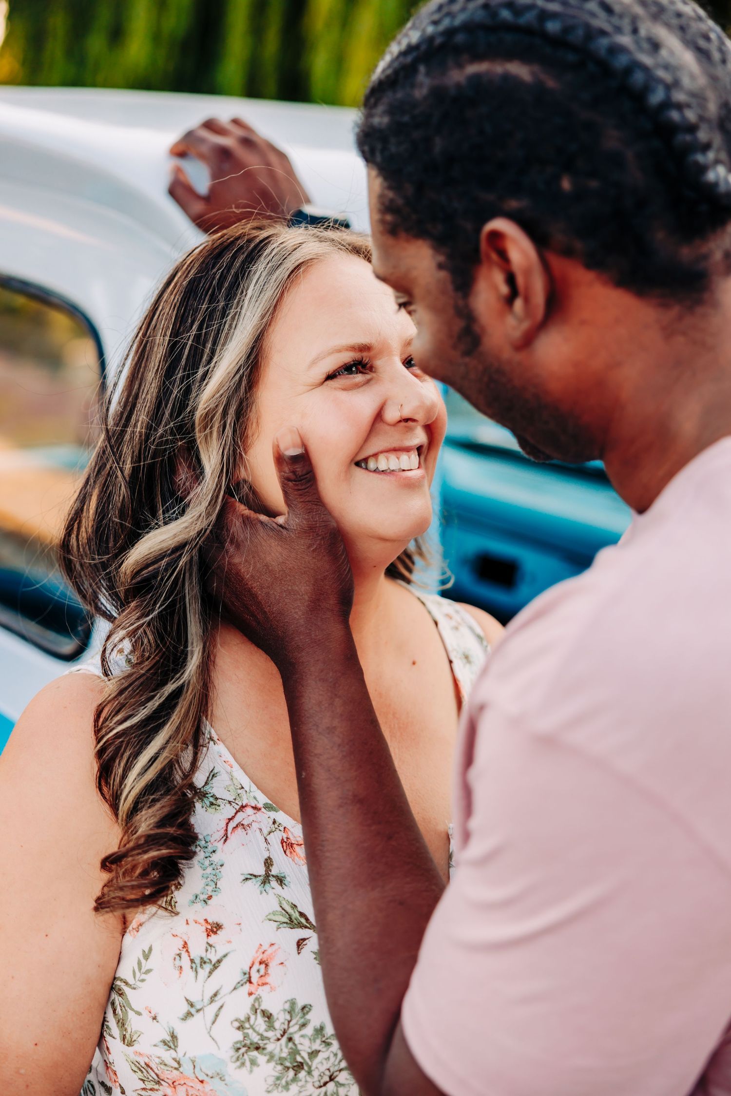 A couple shares intimate laughter and joy while posing together near a vintage blue car.