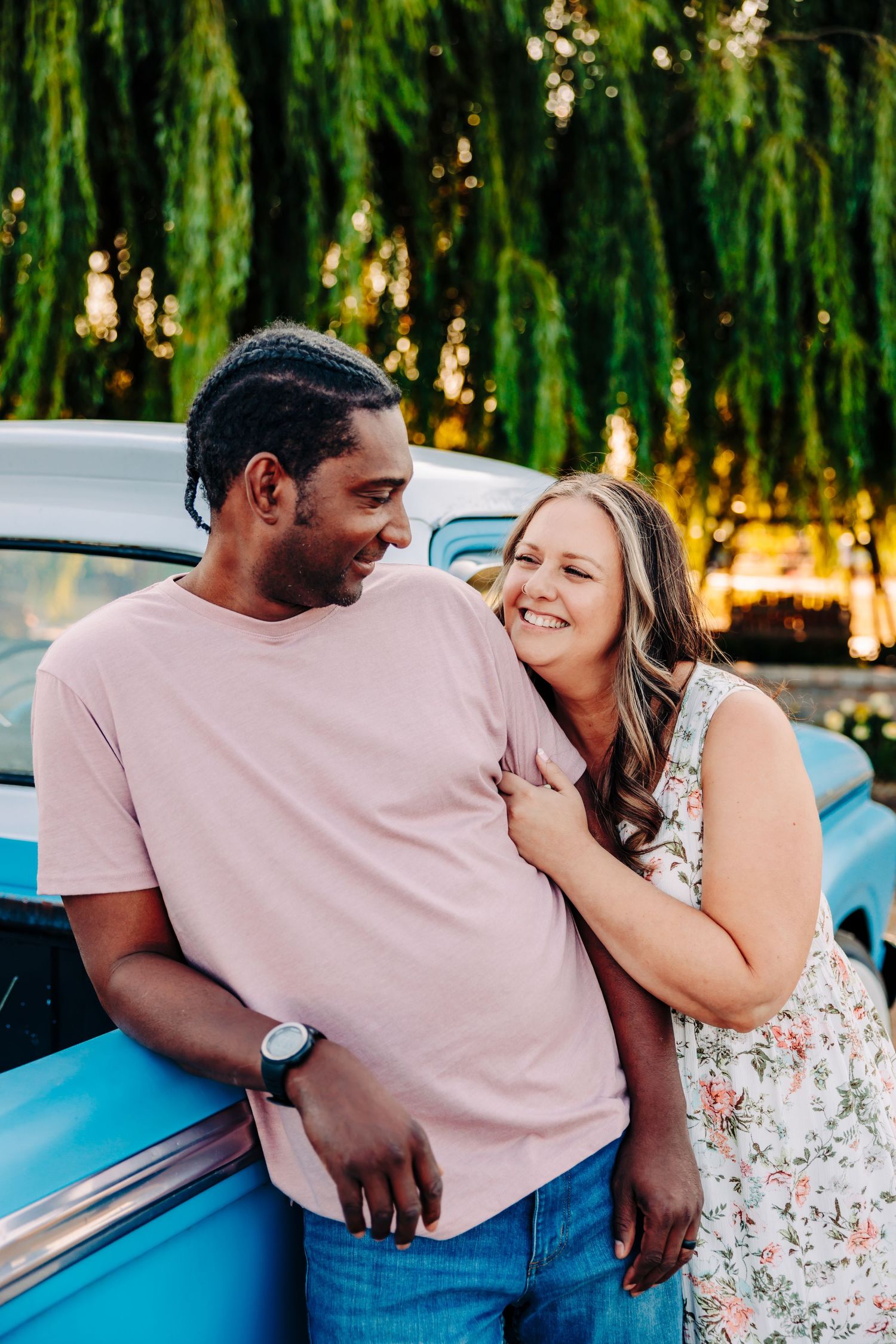 A couple shares intimate moments while leaning against a vintage blue car during a sunset photoshoot.