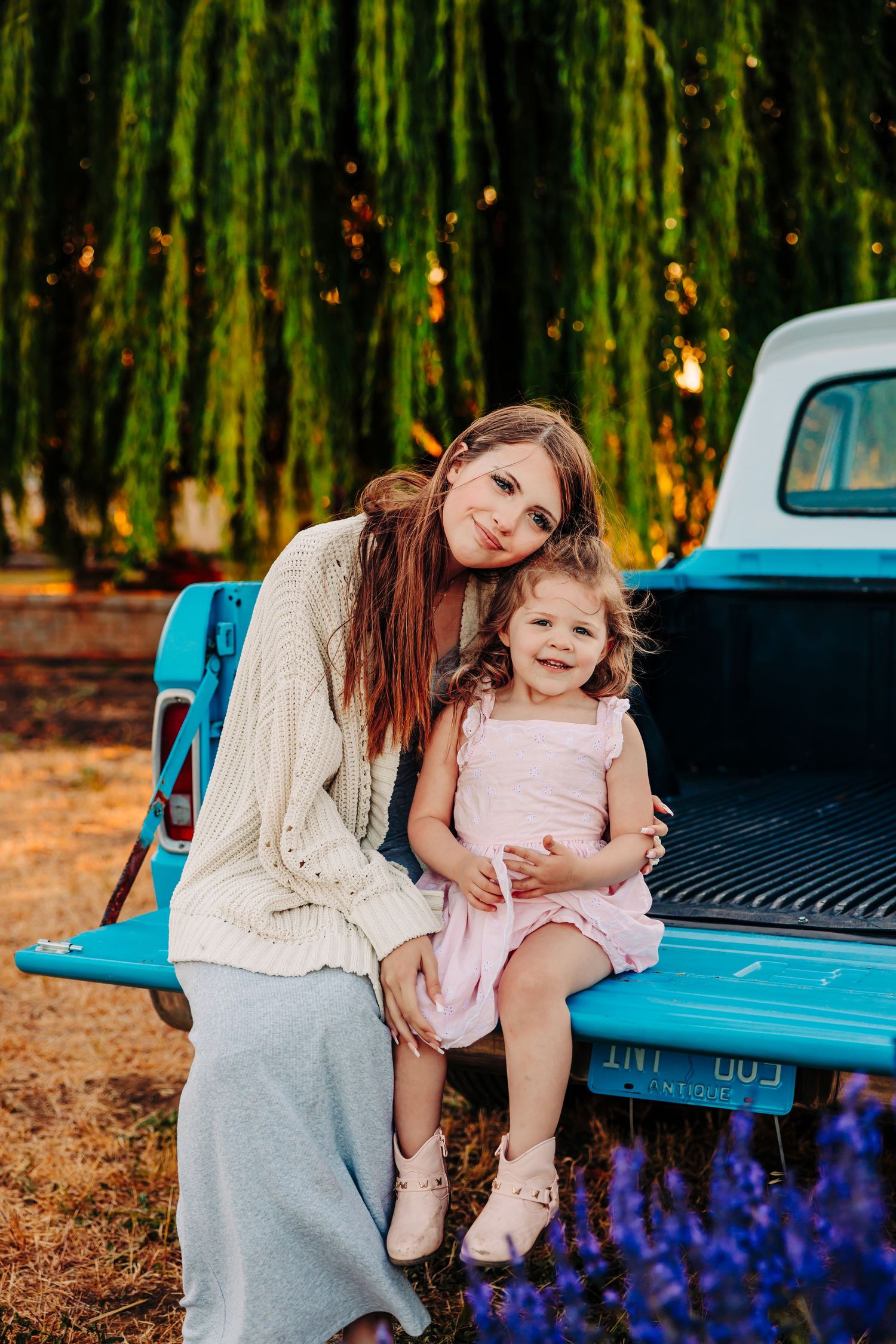 A tender moment shared between parent and child sitting on the tailgate of a vintage blue pickup truck in a wooded setting.