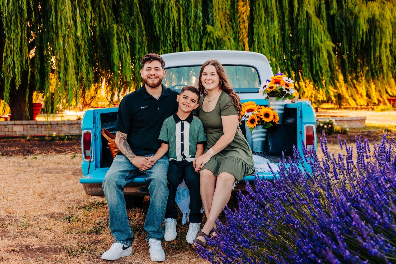 Couple sits on rustic blue truck tailgate surrounded by vibrant purple lavender flowers at sunset.