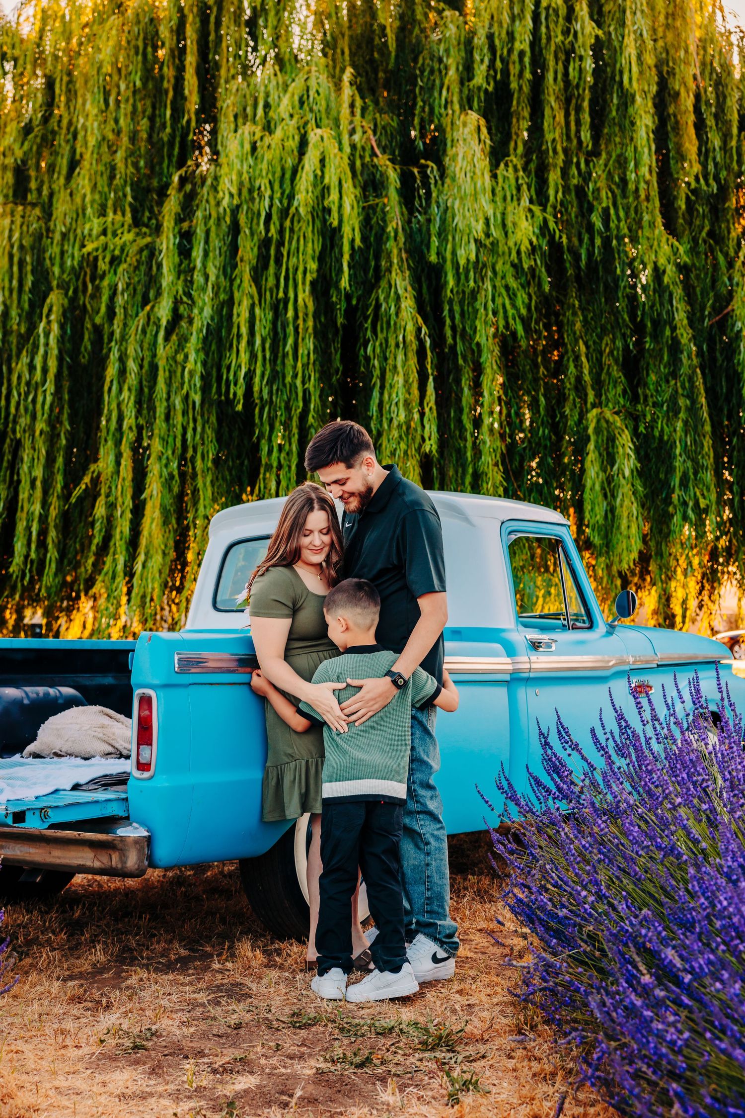 A romantic couple poses near a vintage turquoise pickup truck with blooming purple lavender flowers in the foreground.