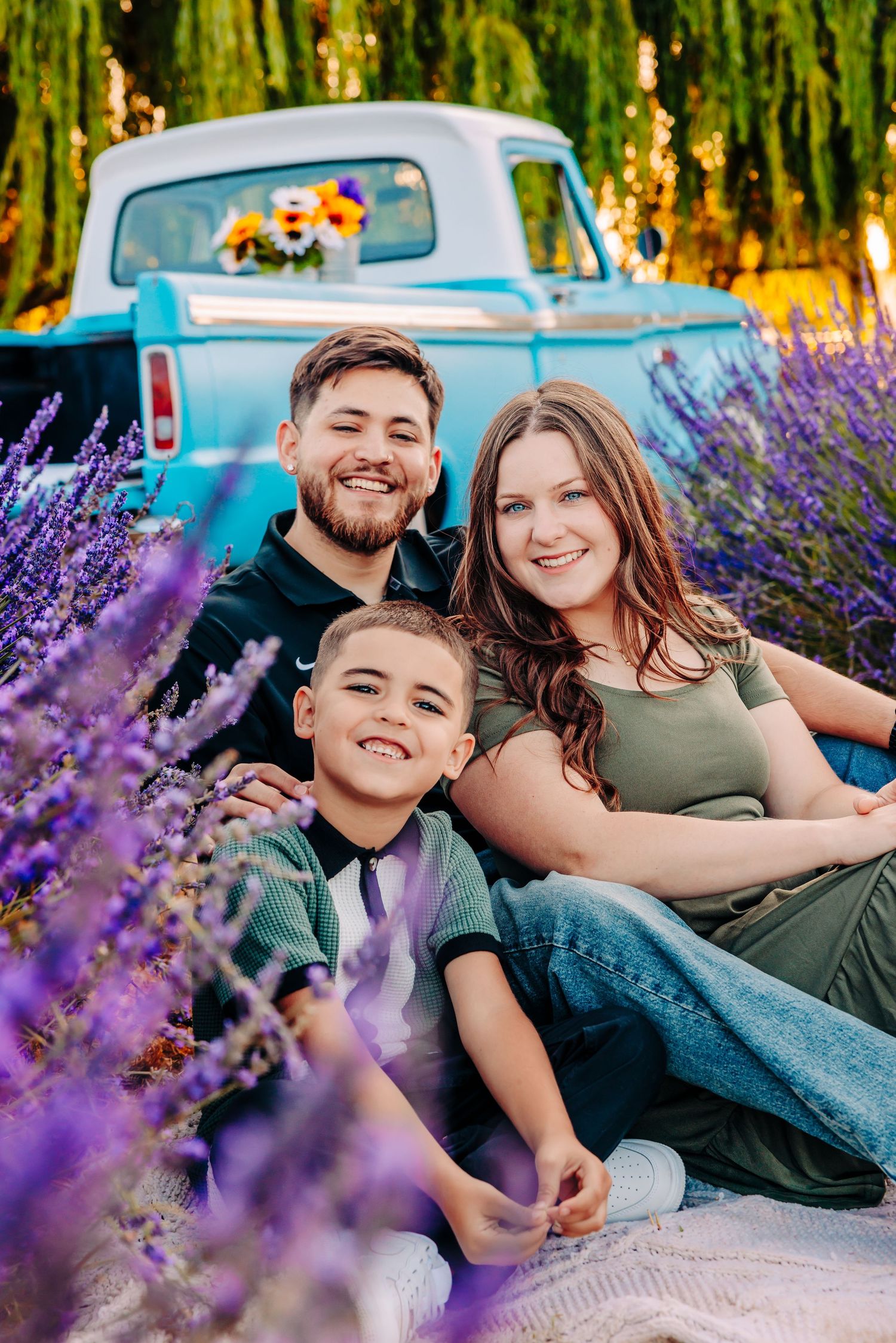 Family sitting together in a lavender field with vintage blue pickup truck in background during golden hour.