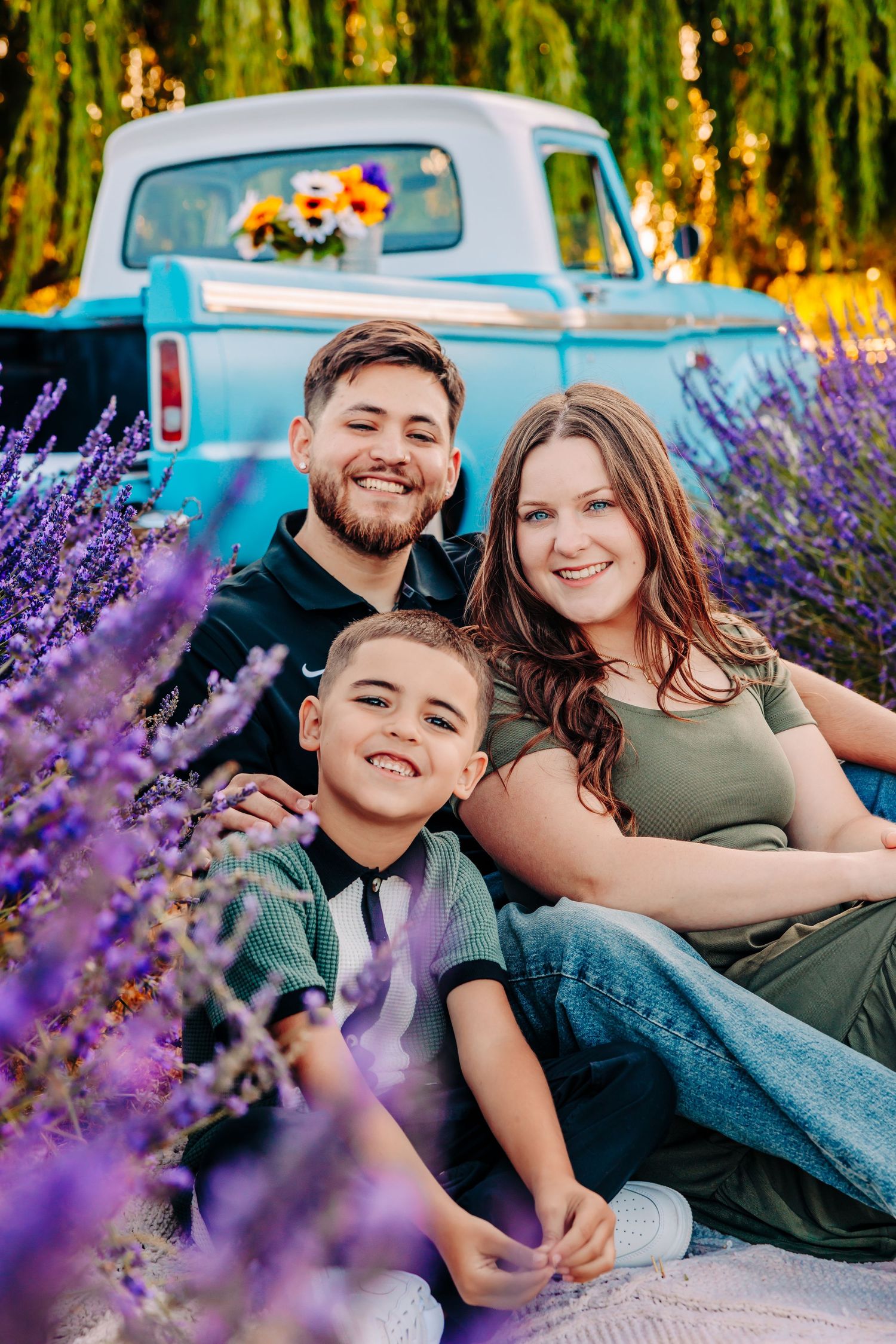 Family poses together in a lavender field next to a vintage blue truck during golden hour sunset.