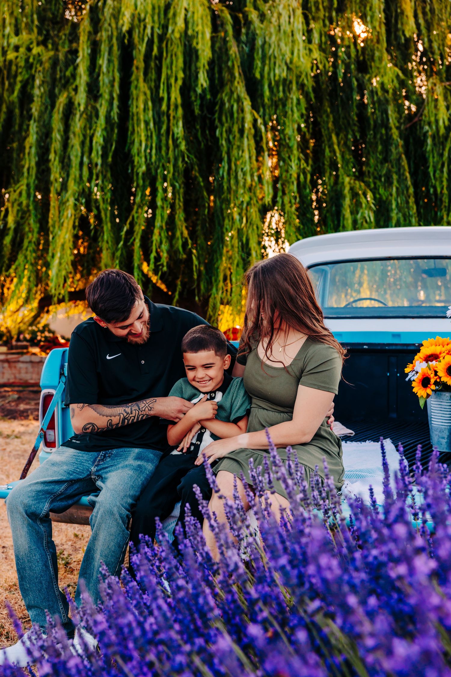 A couple shares tender moments among vibrant purple lavender flowers and willow trees at sunset.