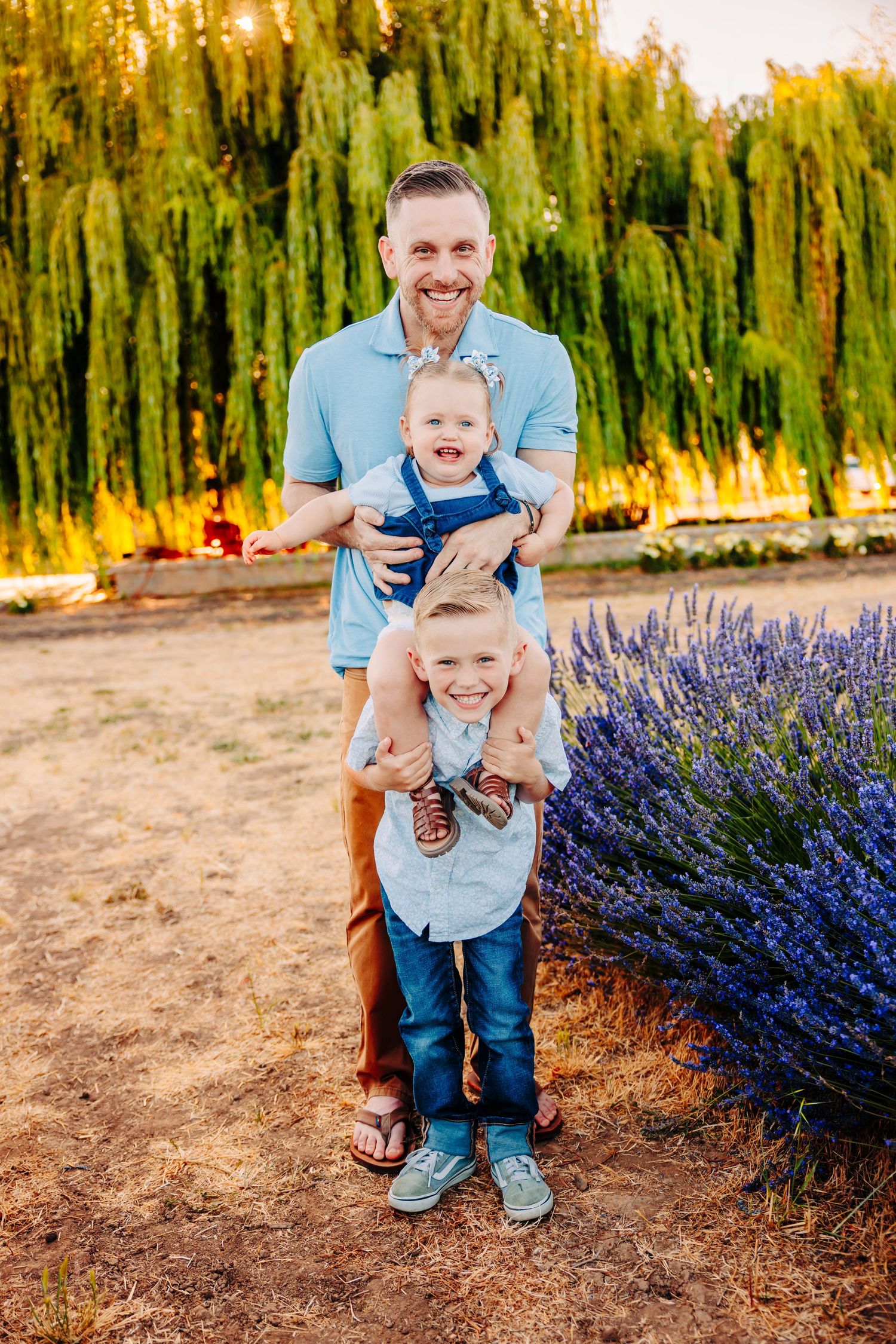 A playful family portrait with weeping willow trees and lavender flowers in the background at golden hour.