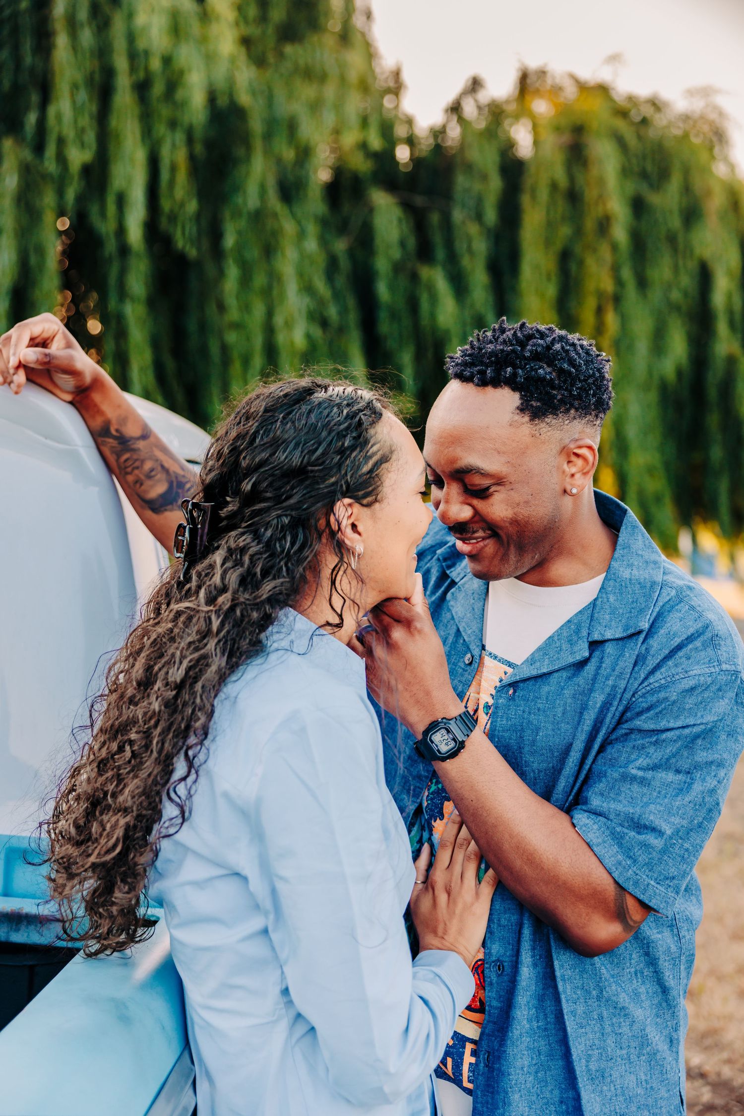 A couple shares intimate moments and laughter while posing together in a lavender field with willow trees behind them.