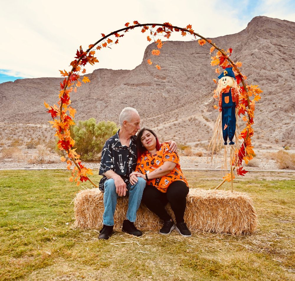 Senior couple sharing romantic moment on hay bale under autumn wreath arch in desert landscape.